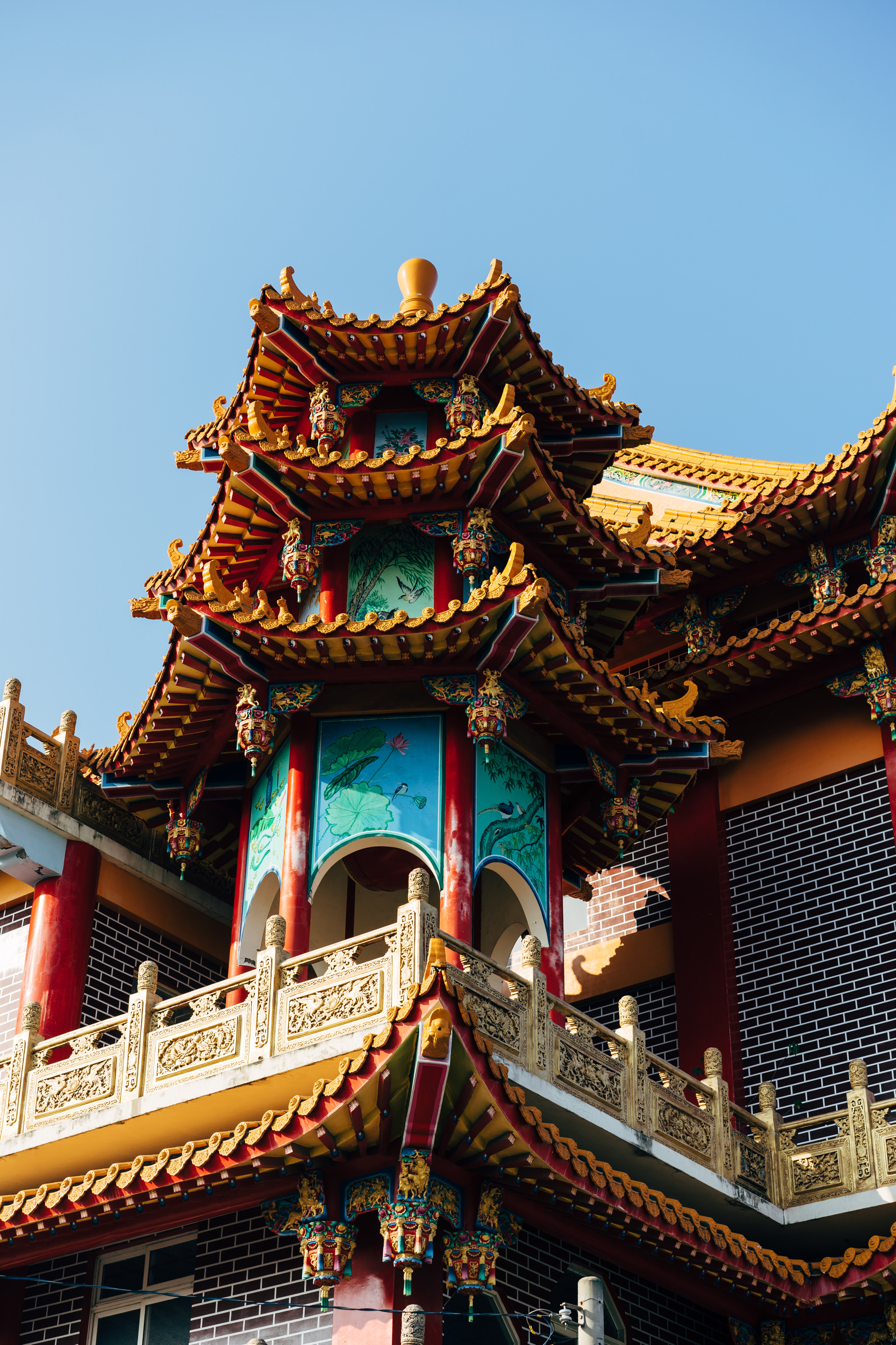 Low-angle view of ornate red and gold Chinese temple roof and balcony.