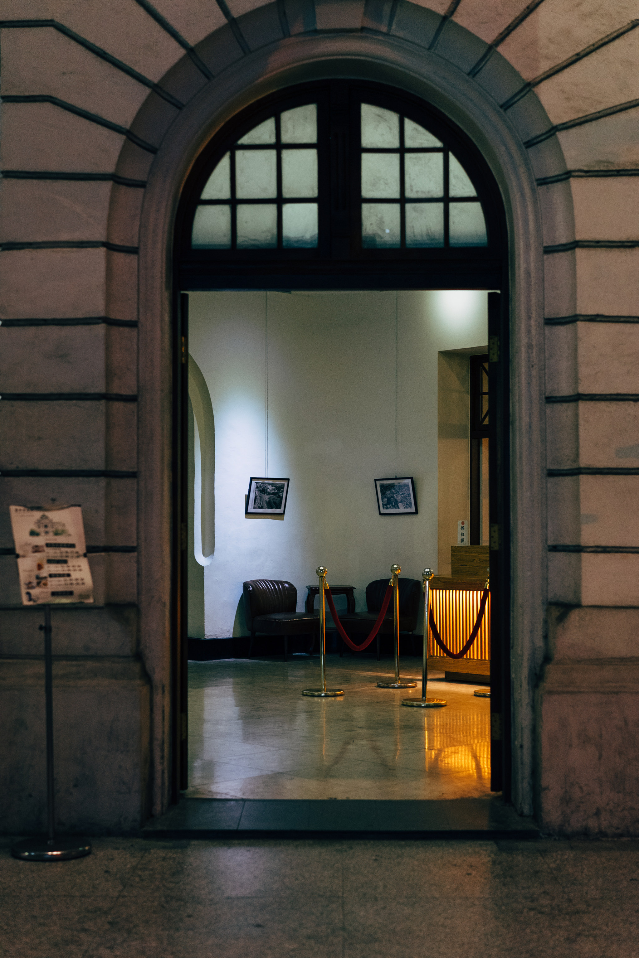 Entrance to a building at night, showing a reception area with two chairs and stanchions.