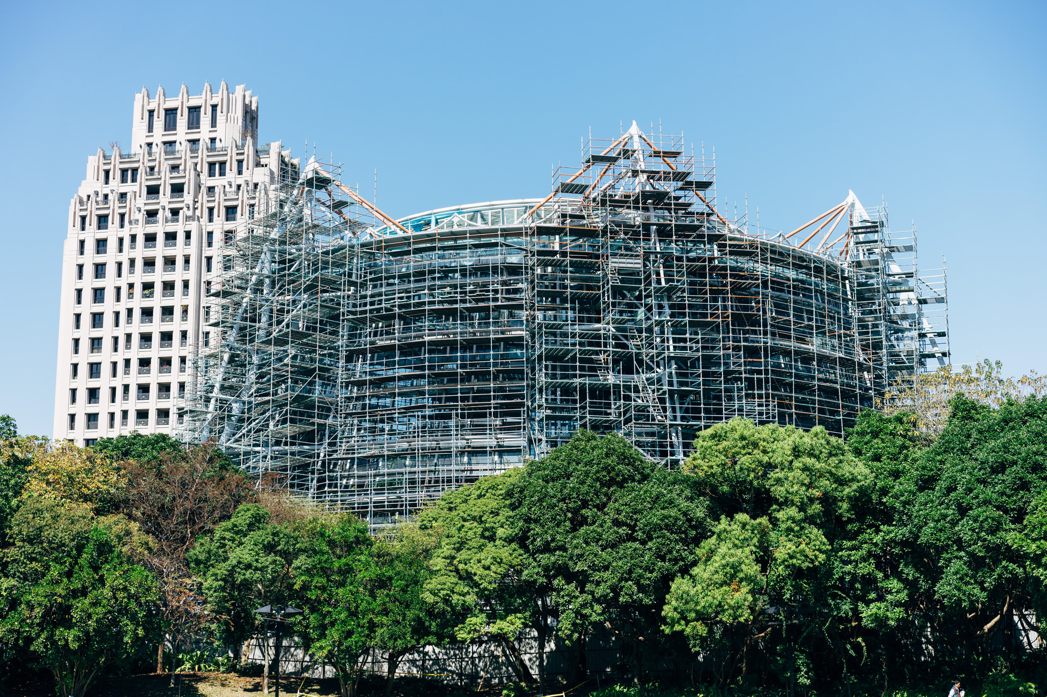 A building under construction in Taichung, Taiwan, surrounded by lush green trees.