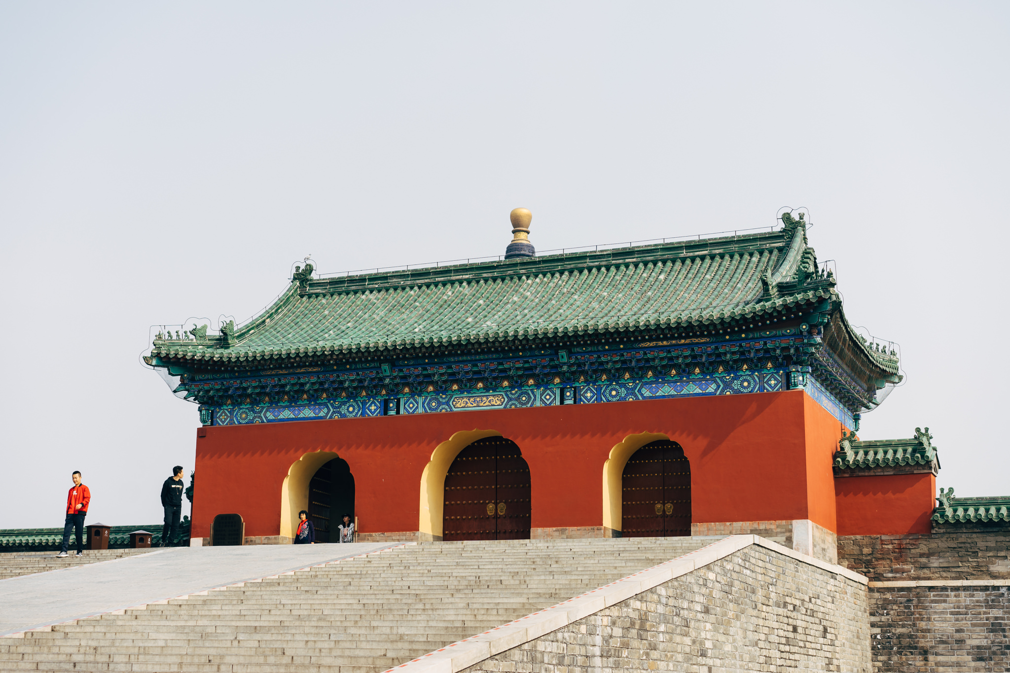 Temple of Heaven gate with green roof and red walls, people walking on steps in front.