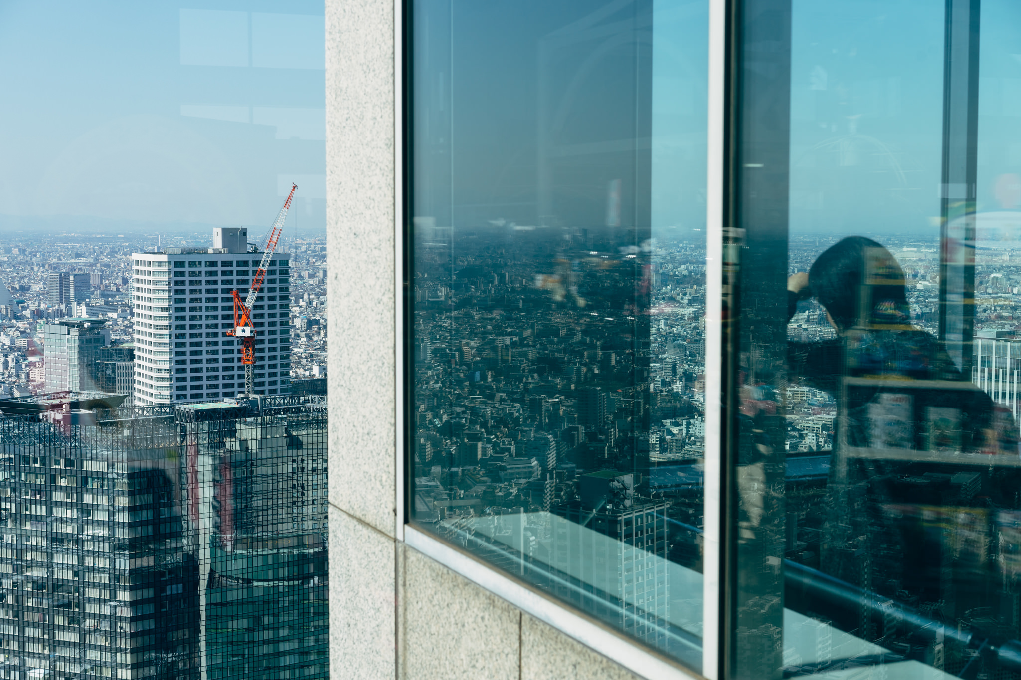 Tokyo cityscape viewed through a skyscraper window, with a construction crane visible.