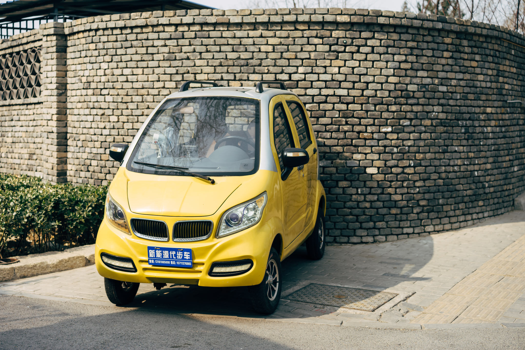 Small yellow car parked next to a brick wall.