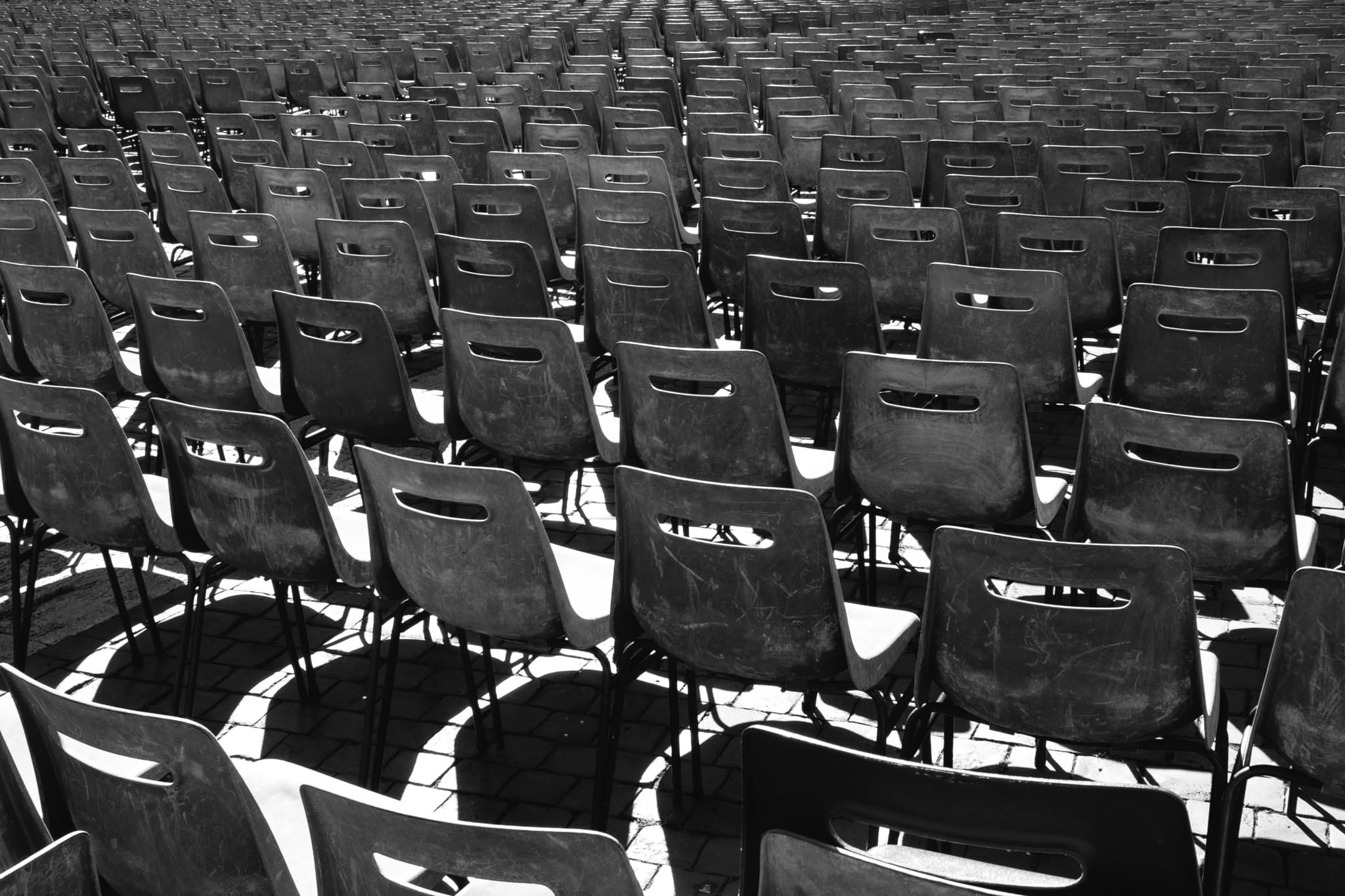 Black and white photo of many empty plastic chairs arranged in rows.