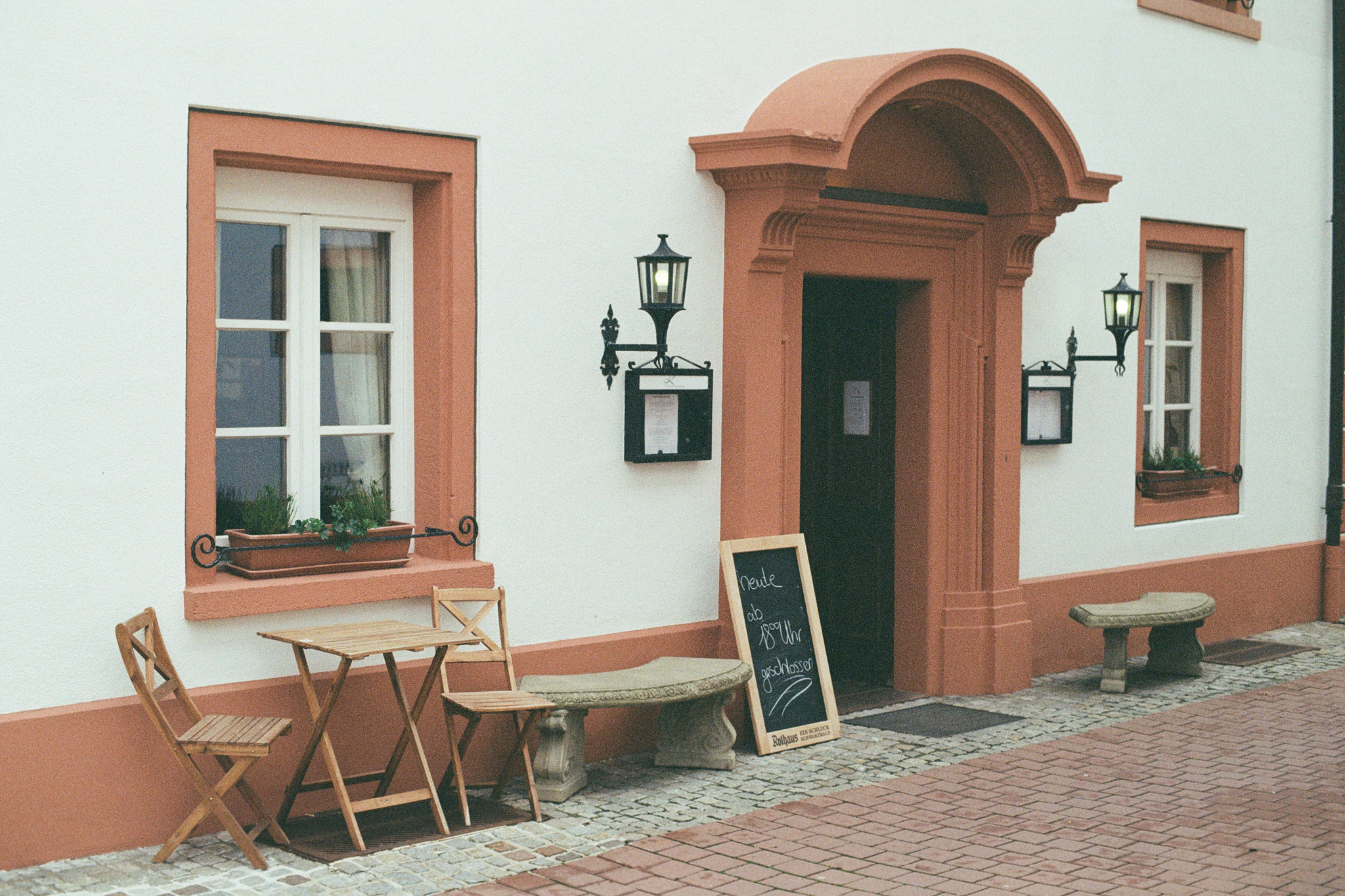 Outdoor cafe scene with a table and chairs in front of a building with peach-colored trim.