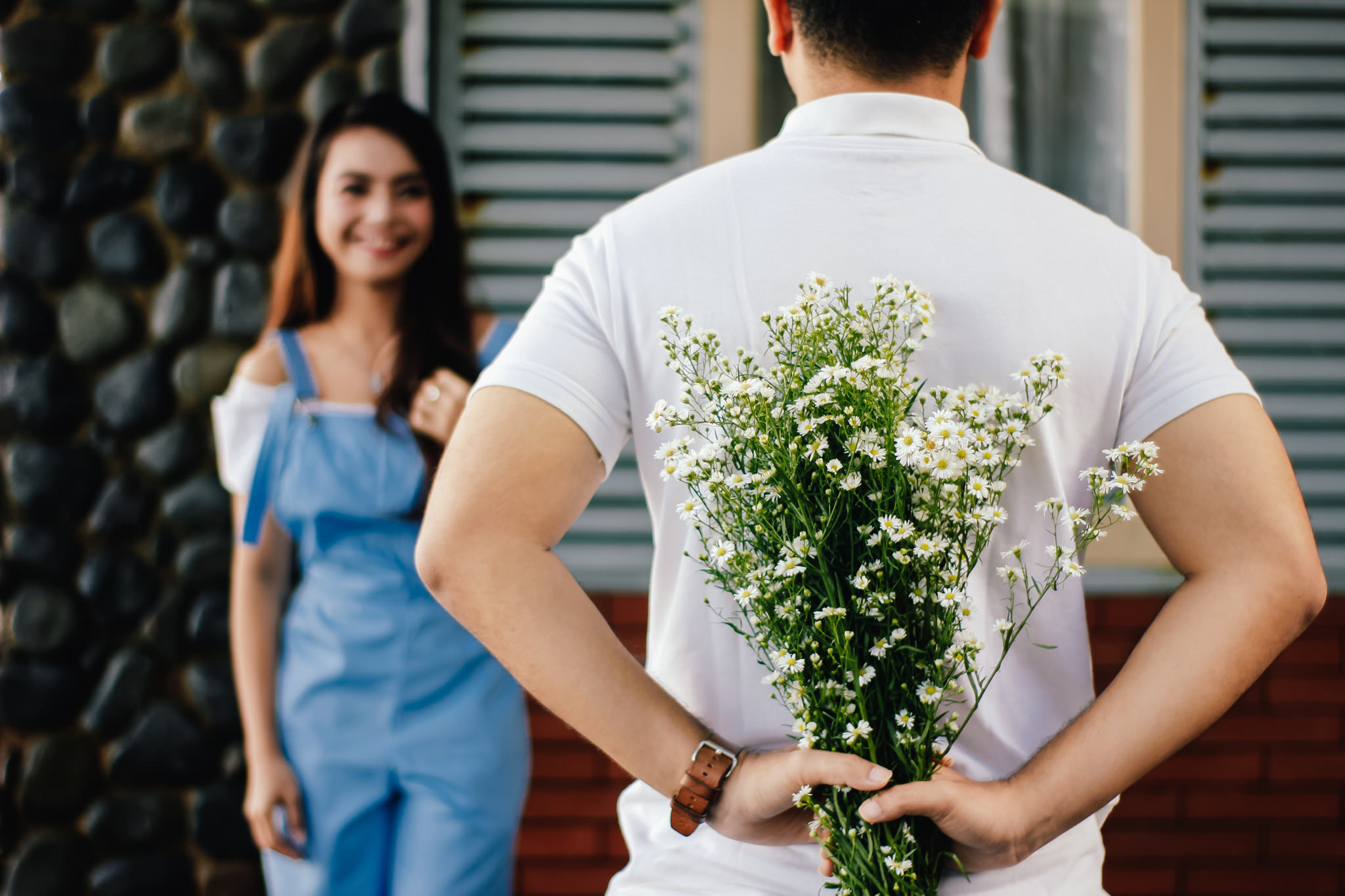 Man hiding flowers behind his back for a woman.