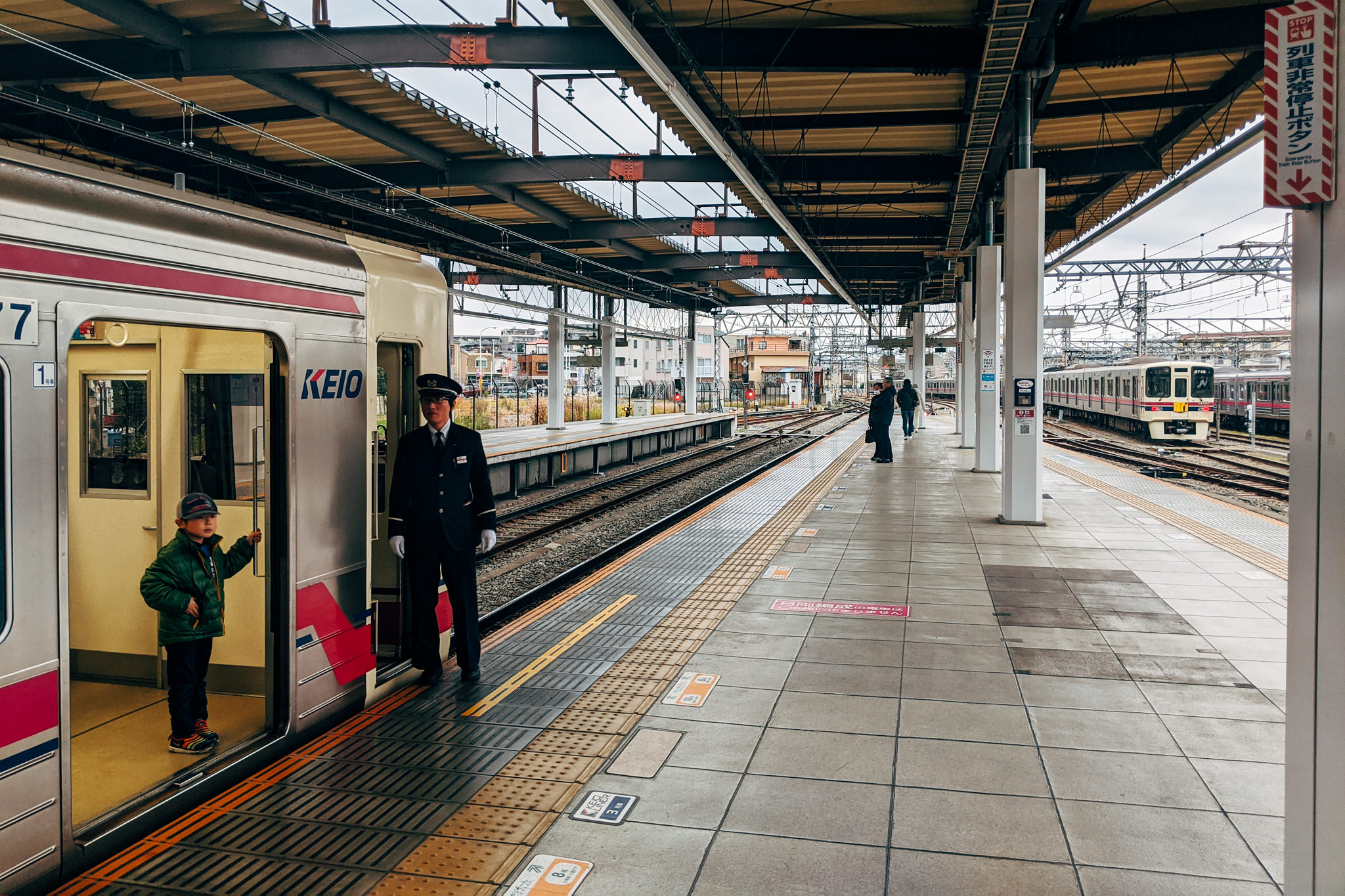 A conductor assists a young boy boarding a Keio train at a station platform.