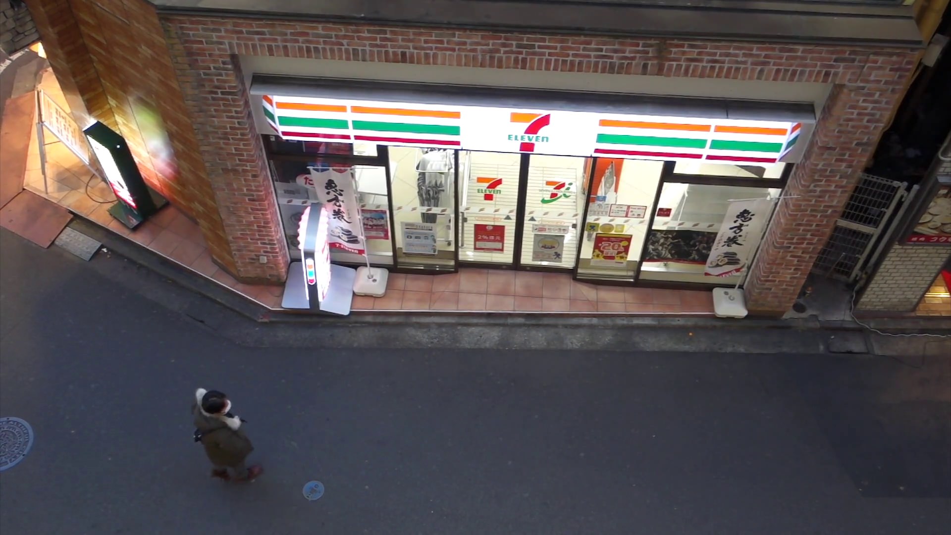 High-angle view of a 7-Eleven convenience store in Japan with a person walking on the street.