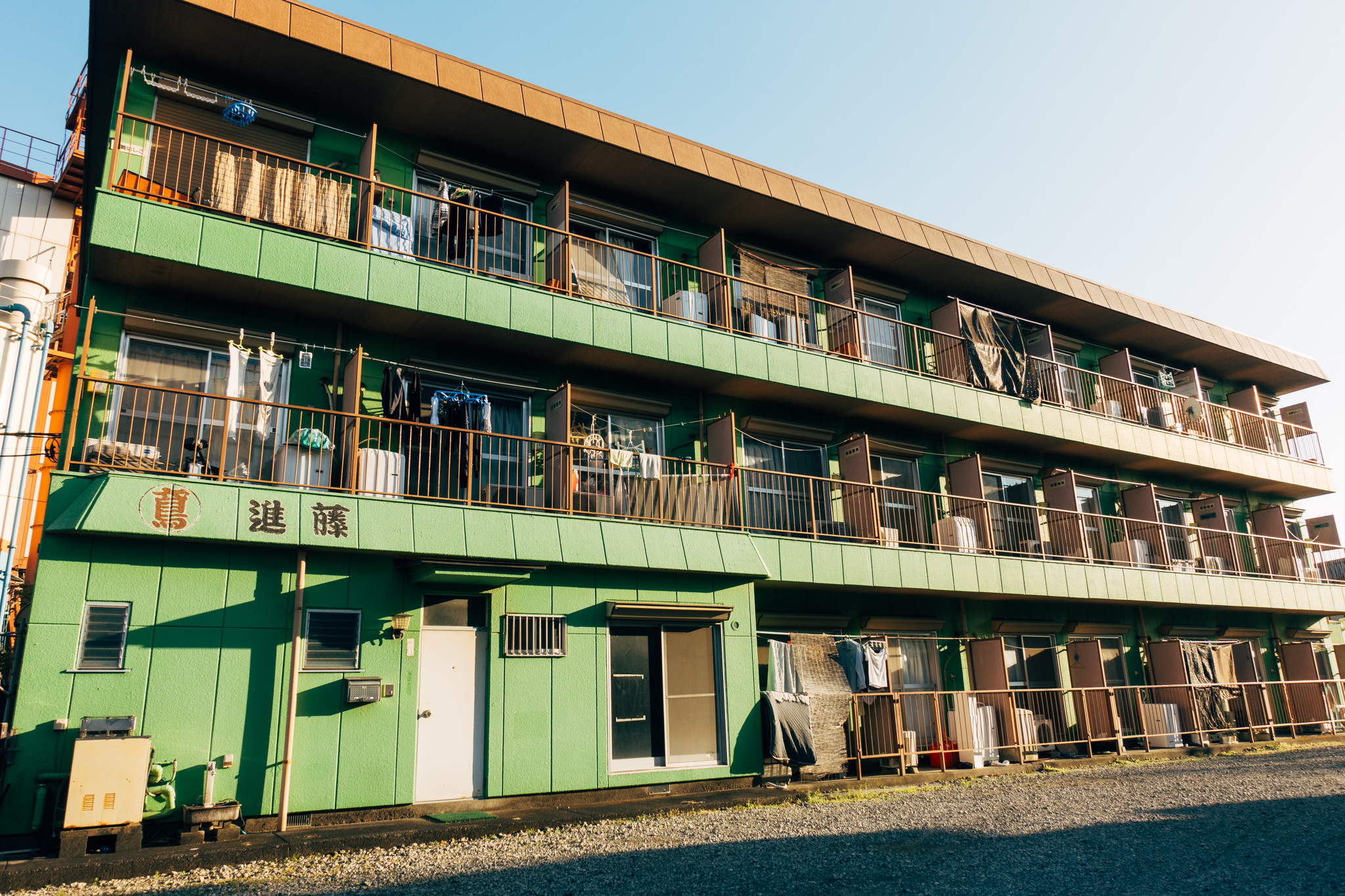 Green apartment building in Tokyo with clothes hanging on balconies.