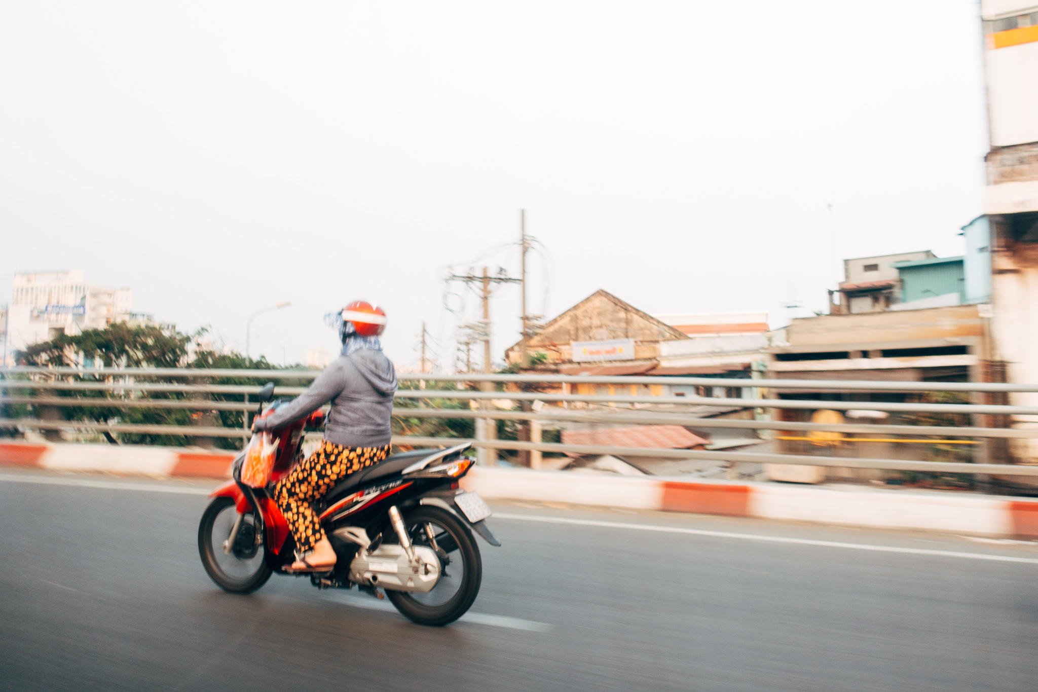 Person wearing a helmet driving a red scooter on a Saigon street.