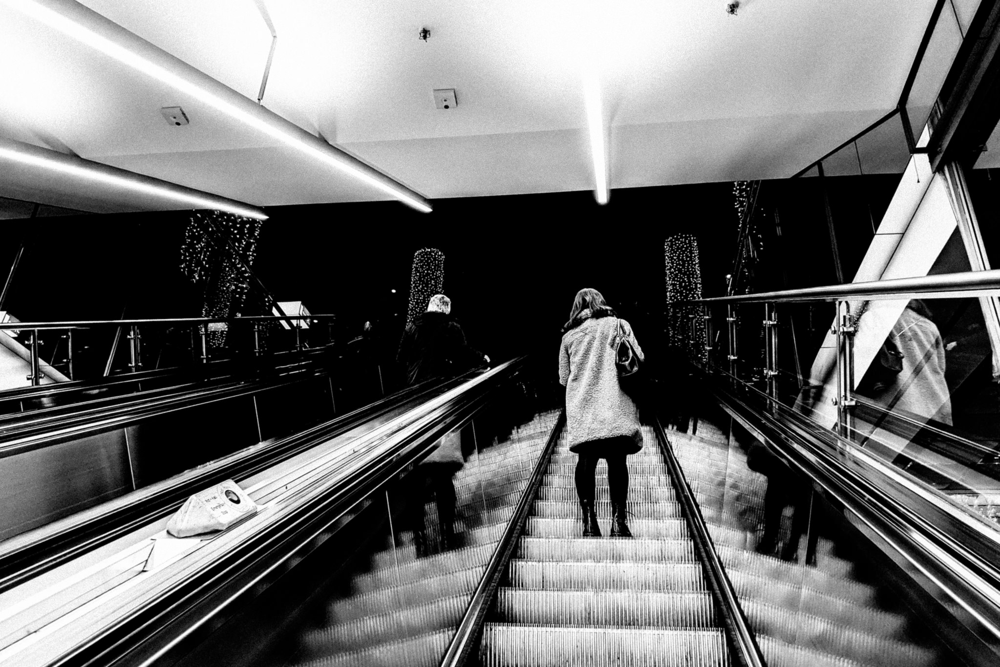 Black and white photo of two people descending an escalator.