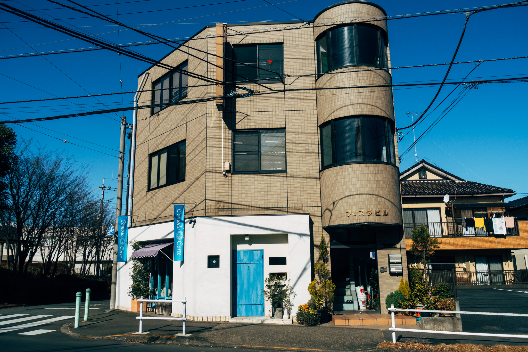 Tokyo street scene with a tan three-story building and a blue door.