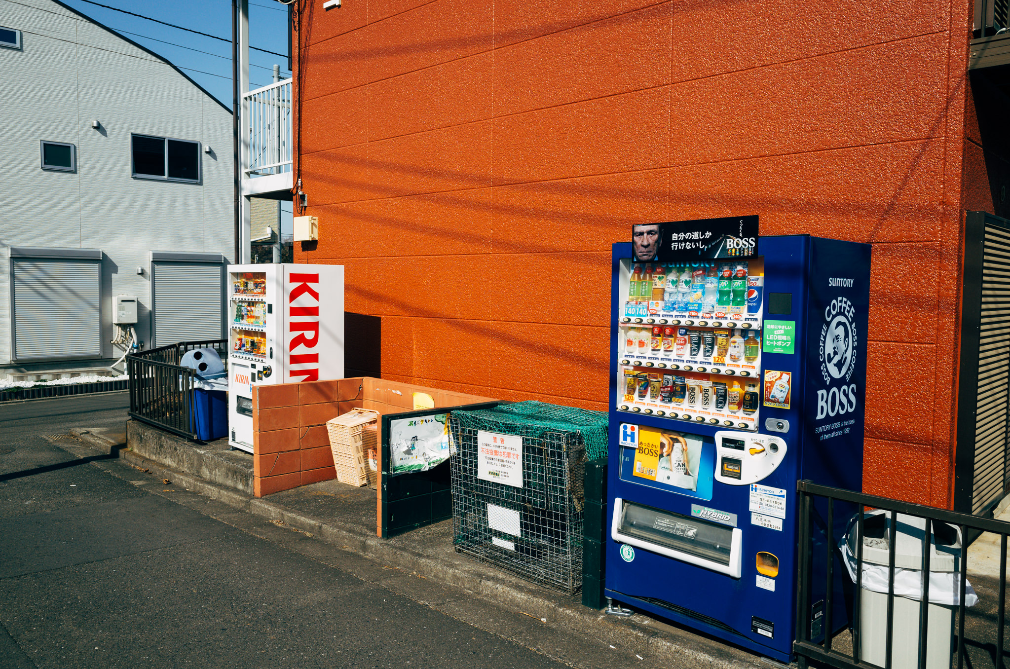 Two Japanese vending machines, one Kirin and one Suntory Boss coffee, against an orange wall.