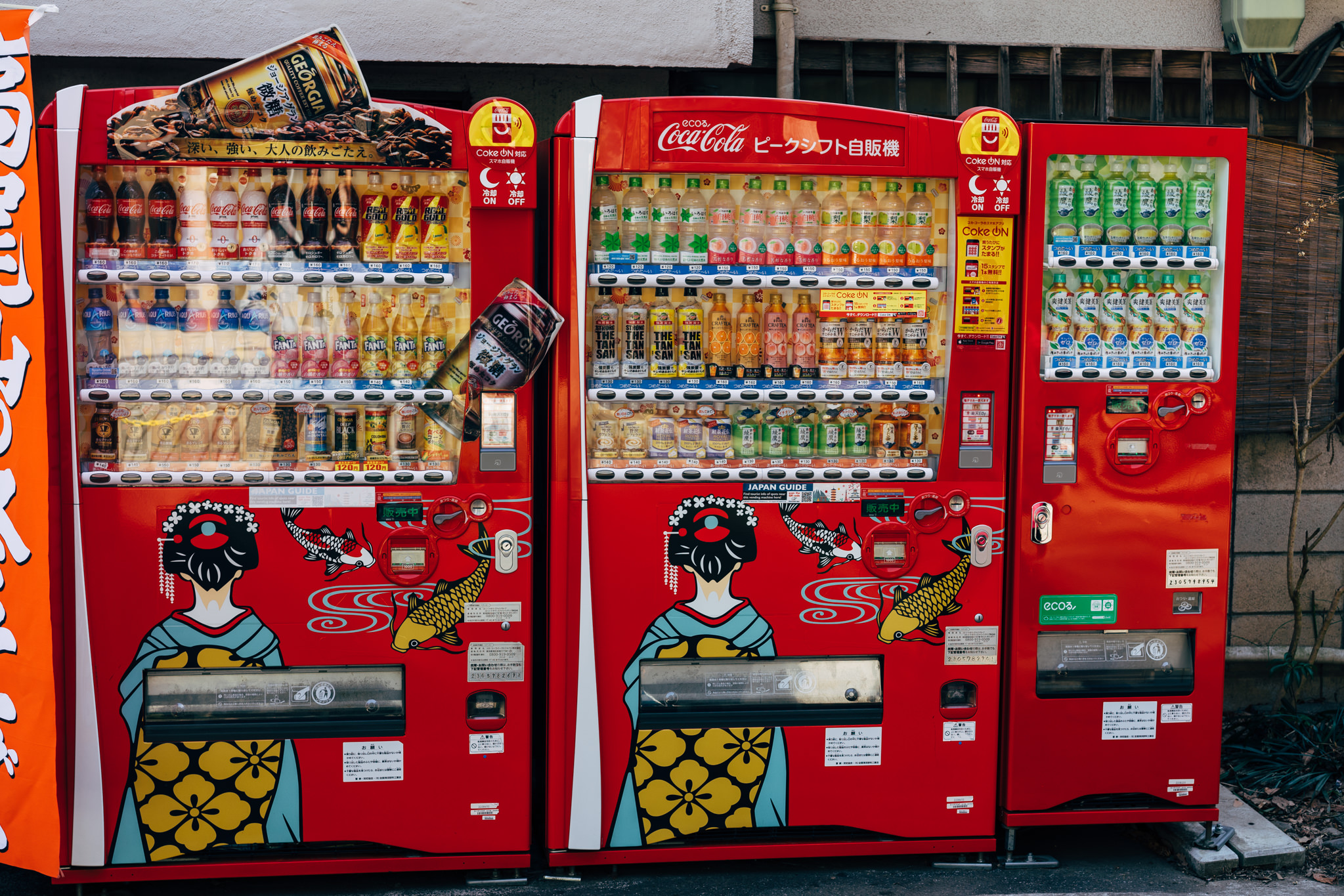 Three red Japanese vending machines stocked with beverages, decorated with geisha and koi fish designs.