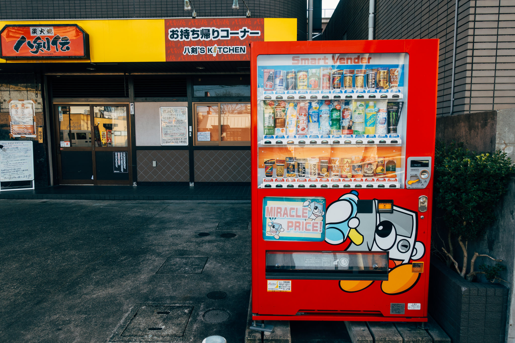 Red Japanese vending machine stocked with drinks, showing a 'miracle price' advertisement.