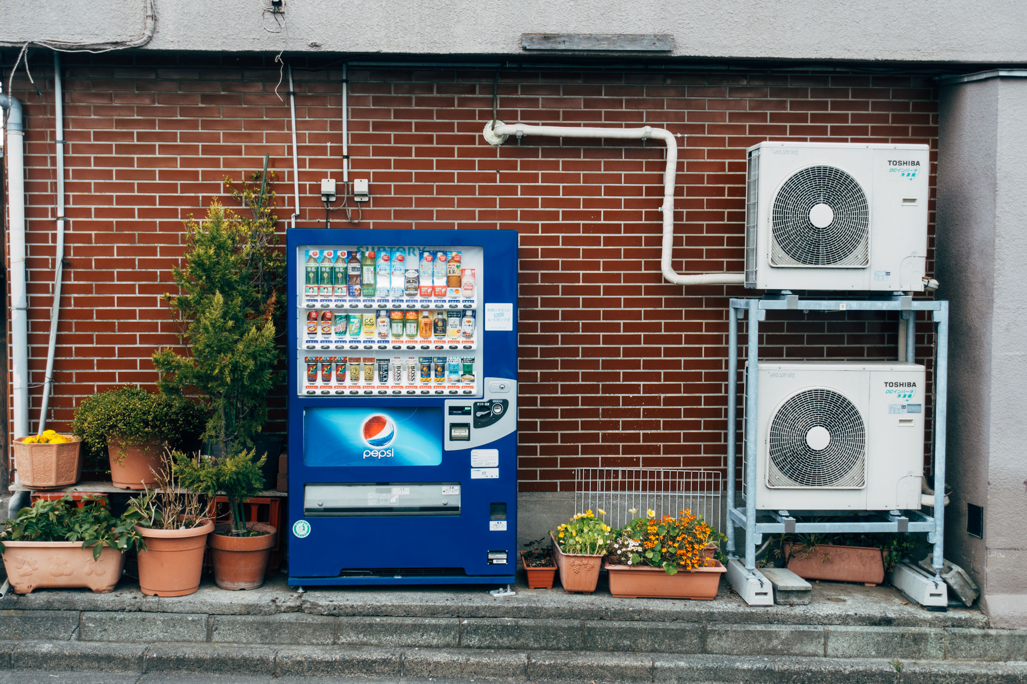 Blue Pepsi vending machine and two Toshiba air conditioning units mounted on a brick wall.