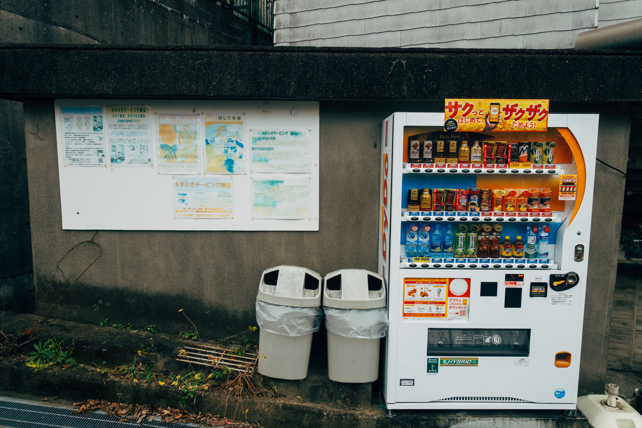 Japanese vending machine stocked with beverages, next to informational posters and trash cans.