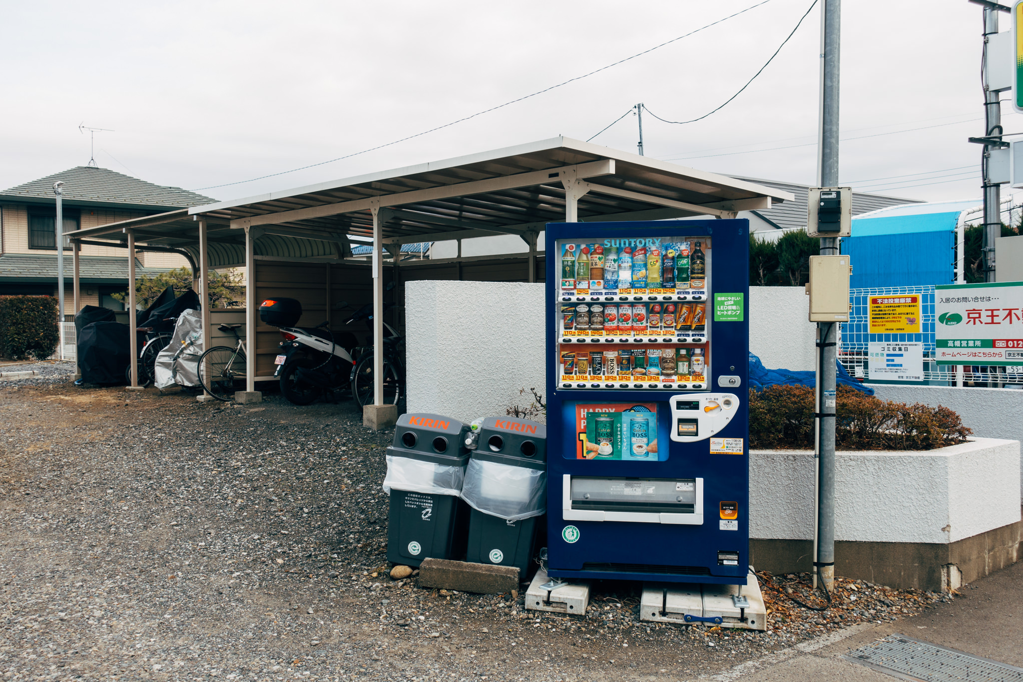 Japanese vending machine stocked with beverages, located under a carport.