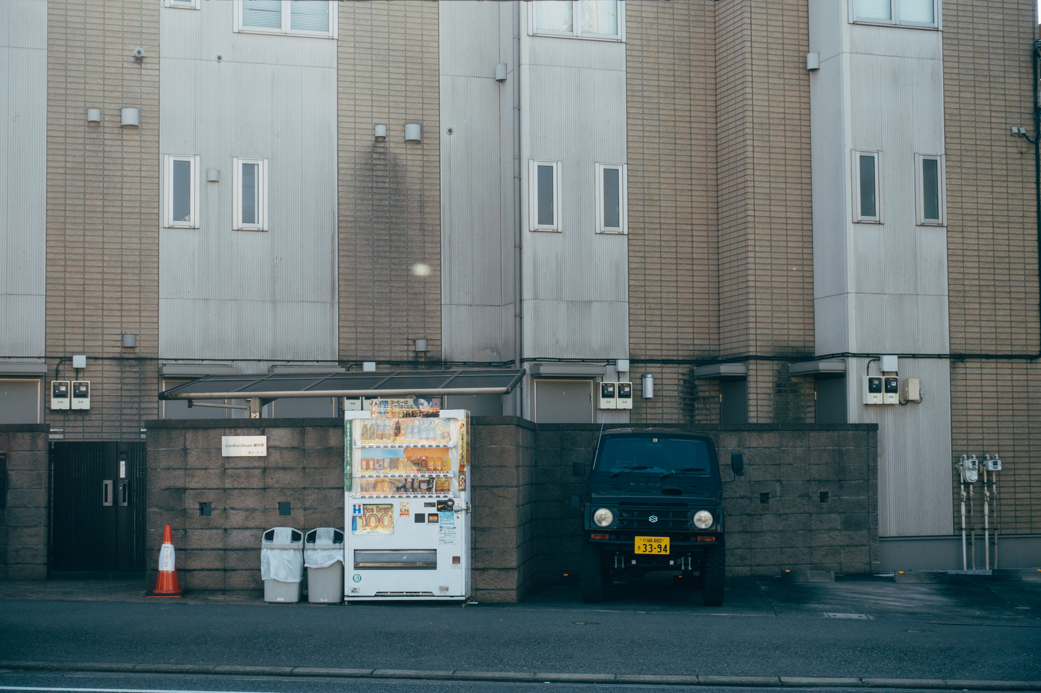 Japanese vending machine and dark-colored vehicle parked in front of a building.