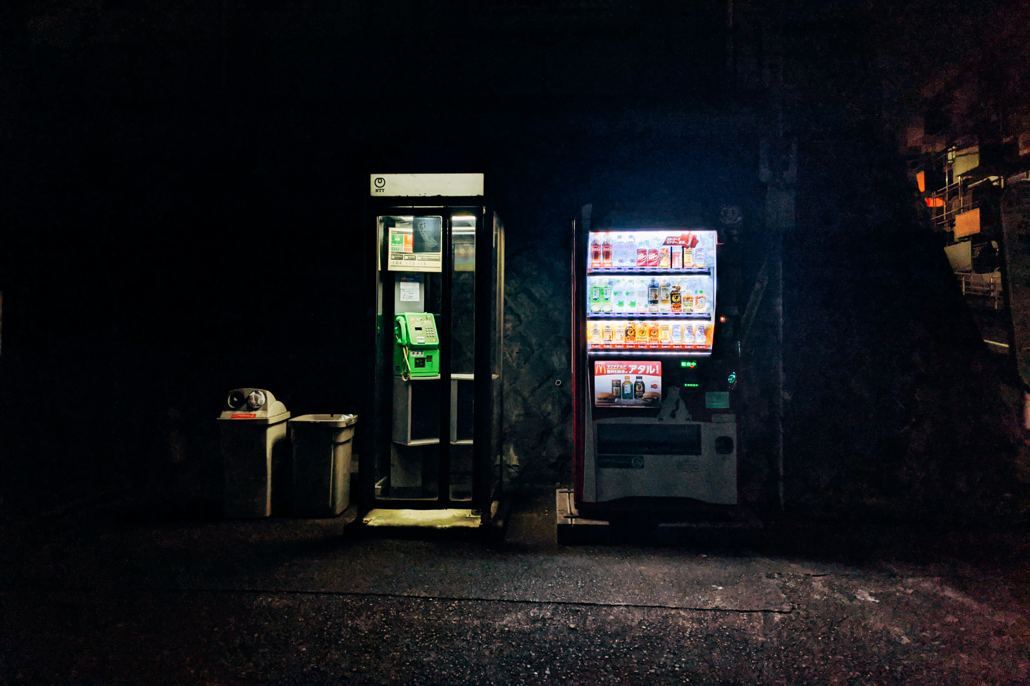 Nighttime view of a payphone and beverage vending machine in Japan.