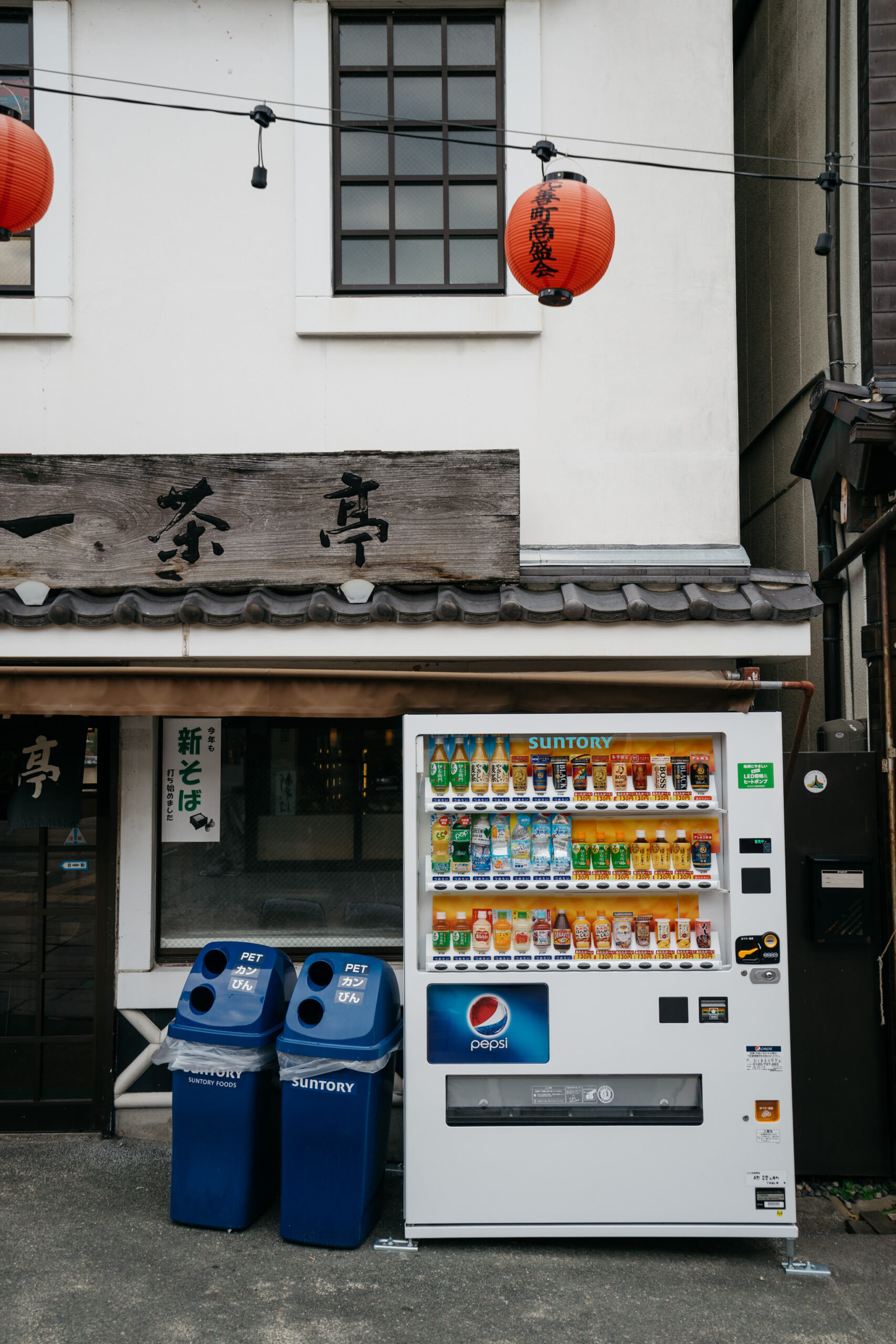 Vending machine with drinks and two blue recycling bins.