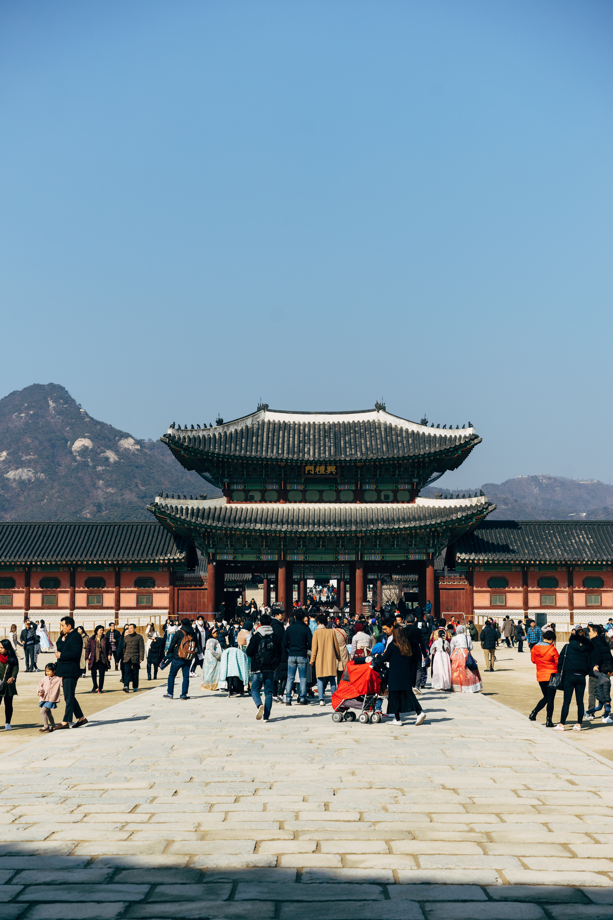 Gyeongbokgung Palace gate with many people walking on a stone courtyard.