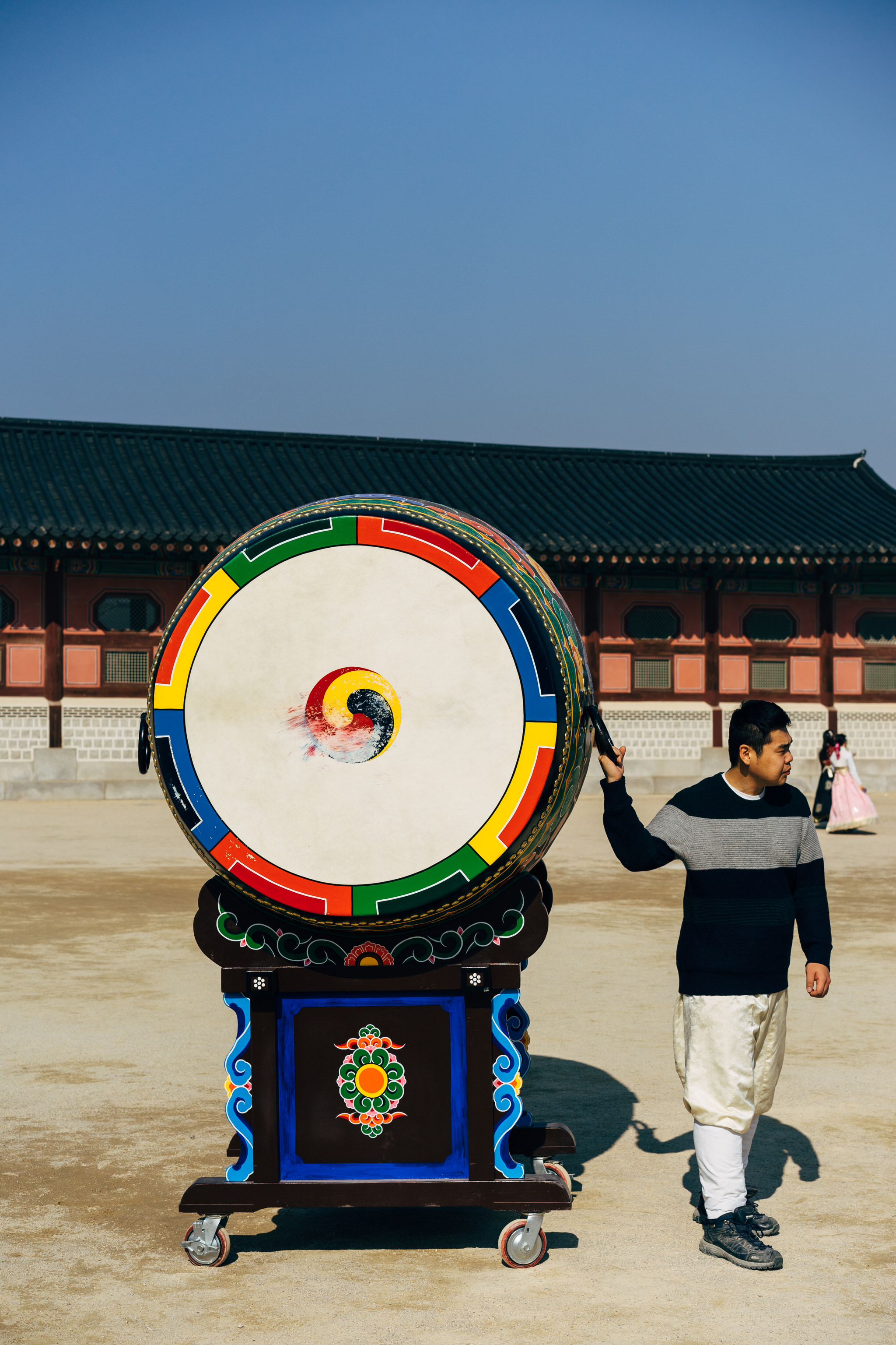 Large colorful Korean drum on wheels with a man in traditional clothing standing beside it at Gyeongbokgung Palace.