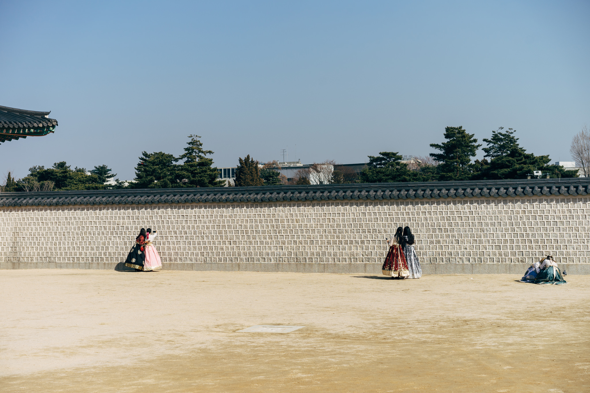 Two groups of people in traditional Korean hanbok dresses stand near a tall stone wall at Gyeongbokgung Palace.