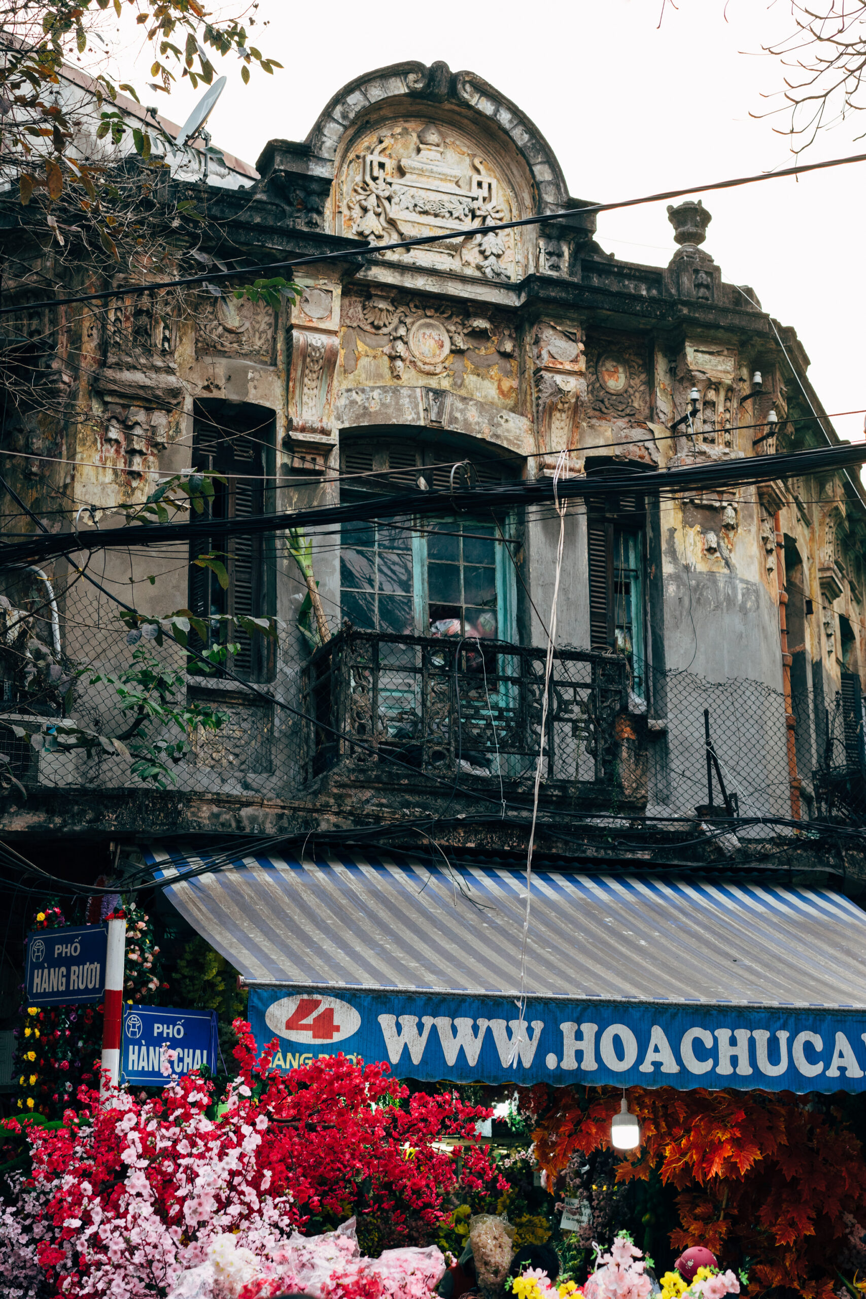 Distressed building facade with ornate details, balcony, and awning; street signs visible below.