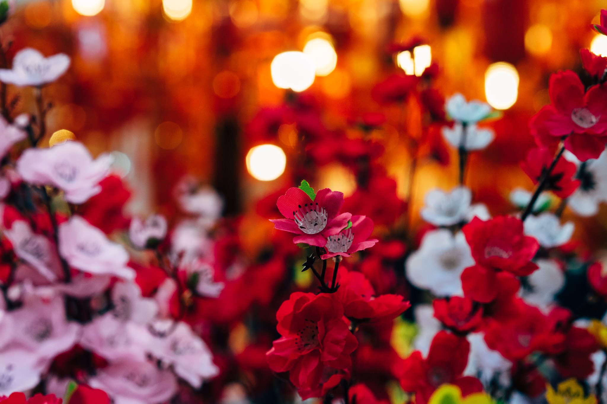 Close-up of red and pink artificial flowers against a blurred orange background.