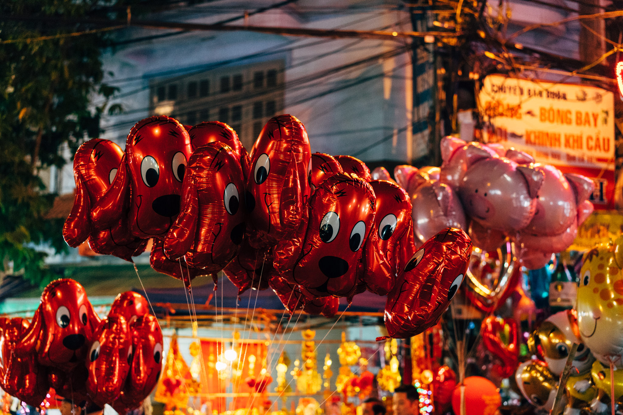 Red balloon dogs and other balloons at a night market.