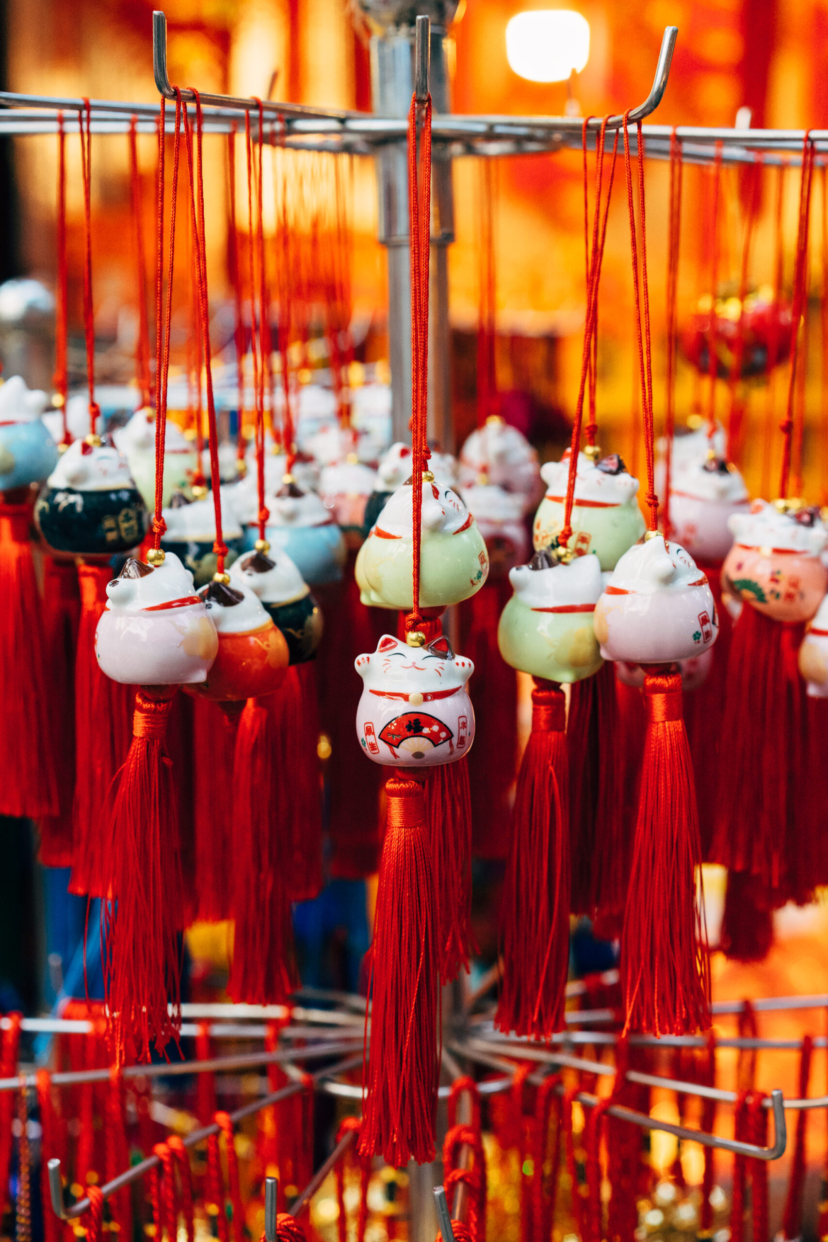 Many Maneki-neko figurines with red tassels hanging from a display.