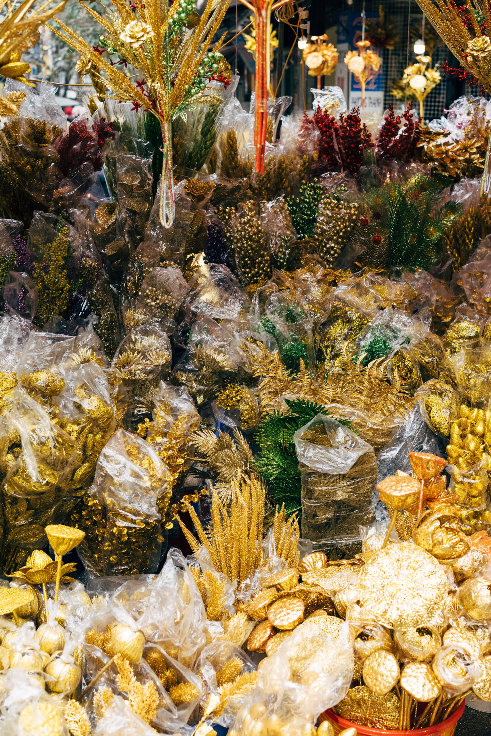 Many gold and green glittery artificial flowers and plants in plastic bags at a market stall.