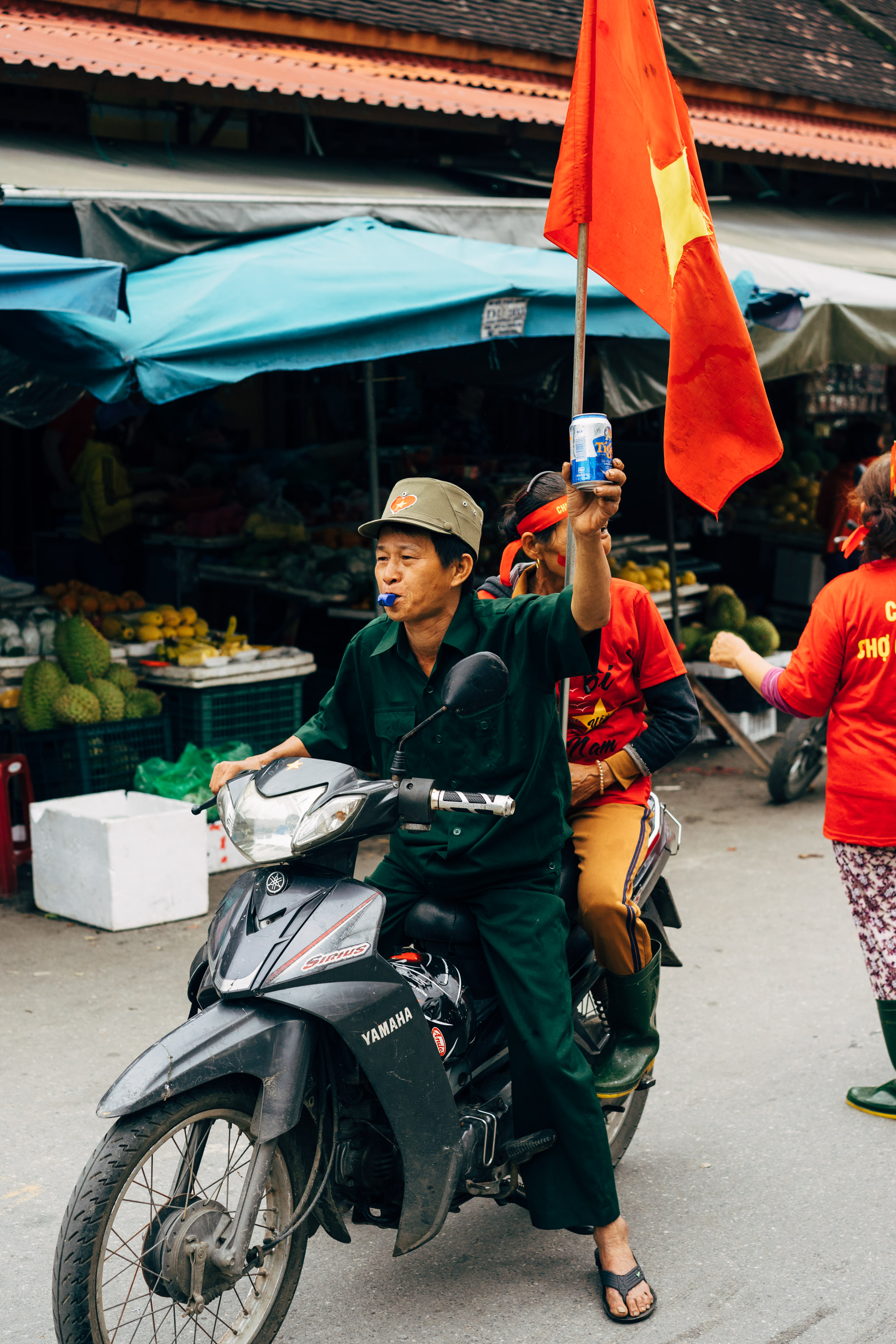 Man on motorbike holding beer and Vietnamese flag.