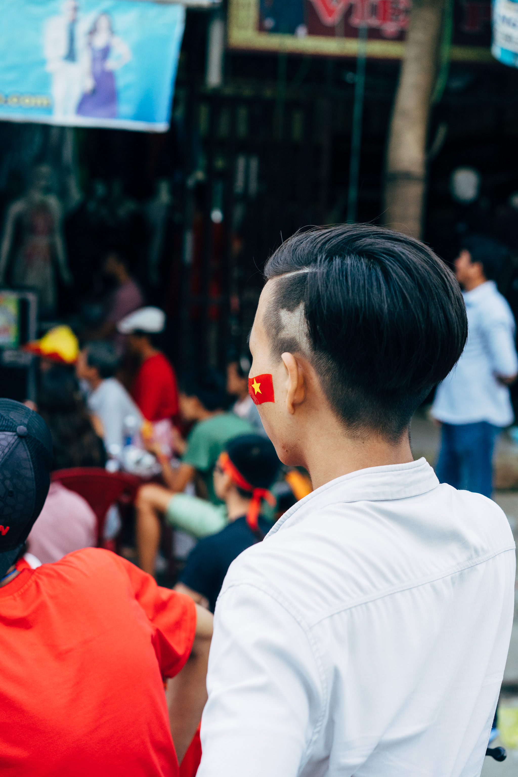Person with Vietnamese flag shaved into their hair and painted on their cheek, among a crowd of soccer fans.