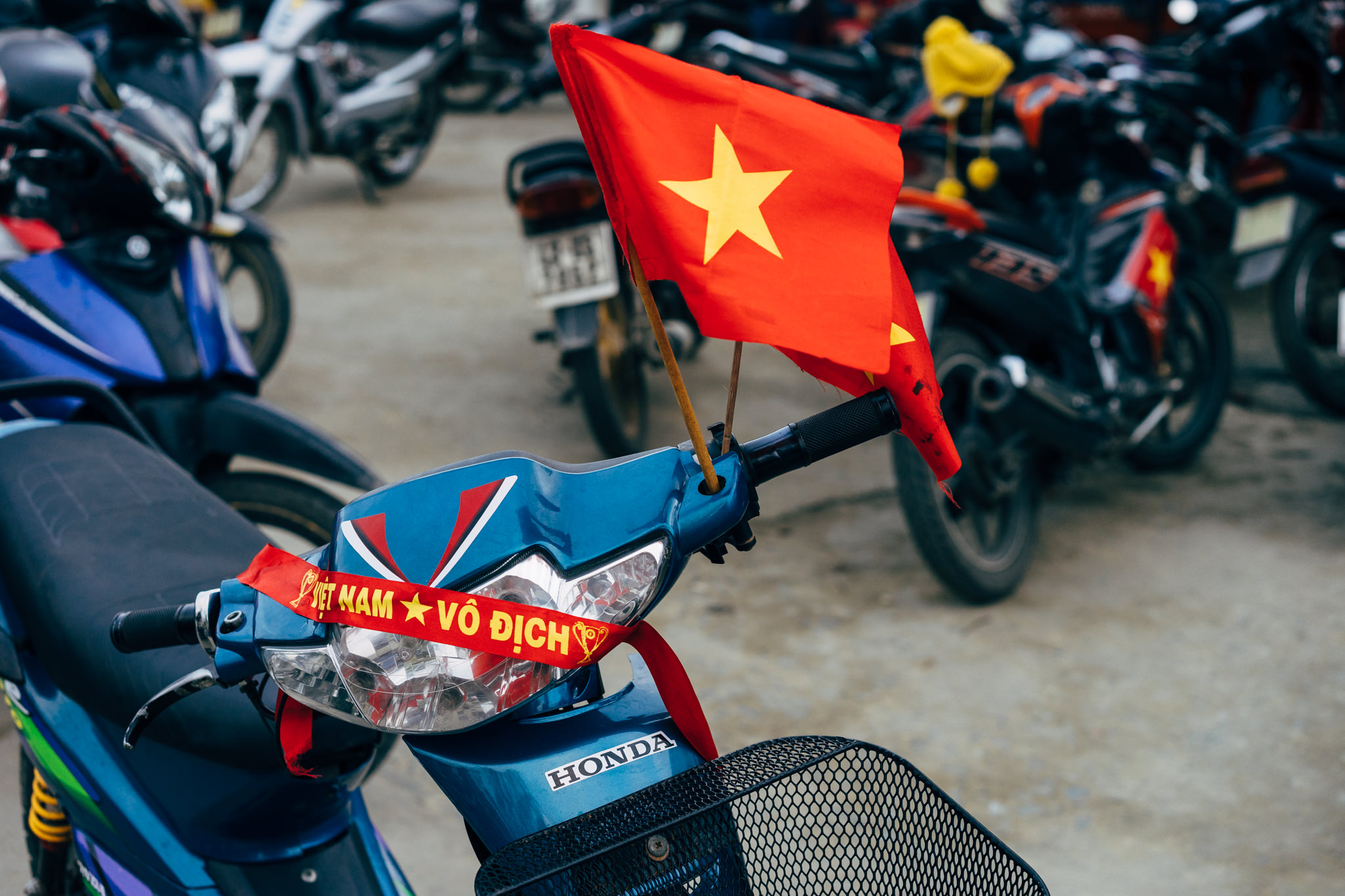 Blue Honda motorbike decorated with a Vietnamese flag and a red ribbon reading 'Viet Nam Vo Dich'.