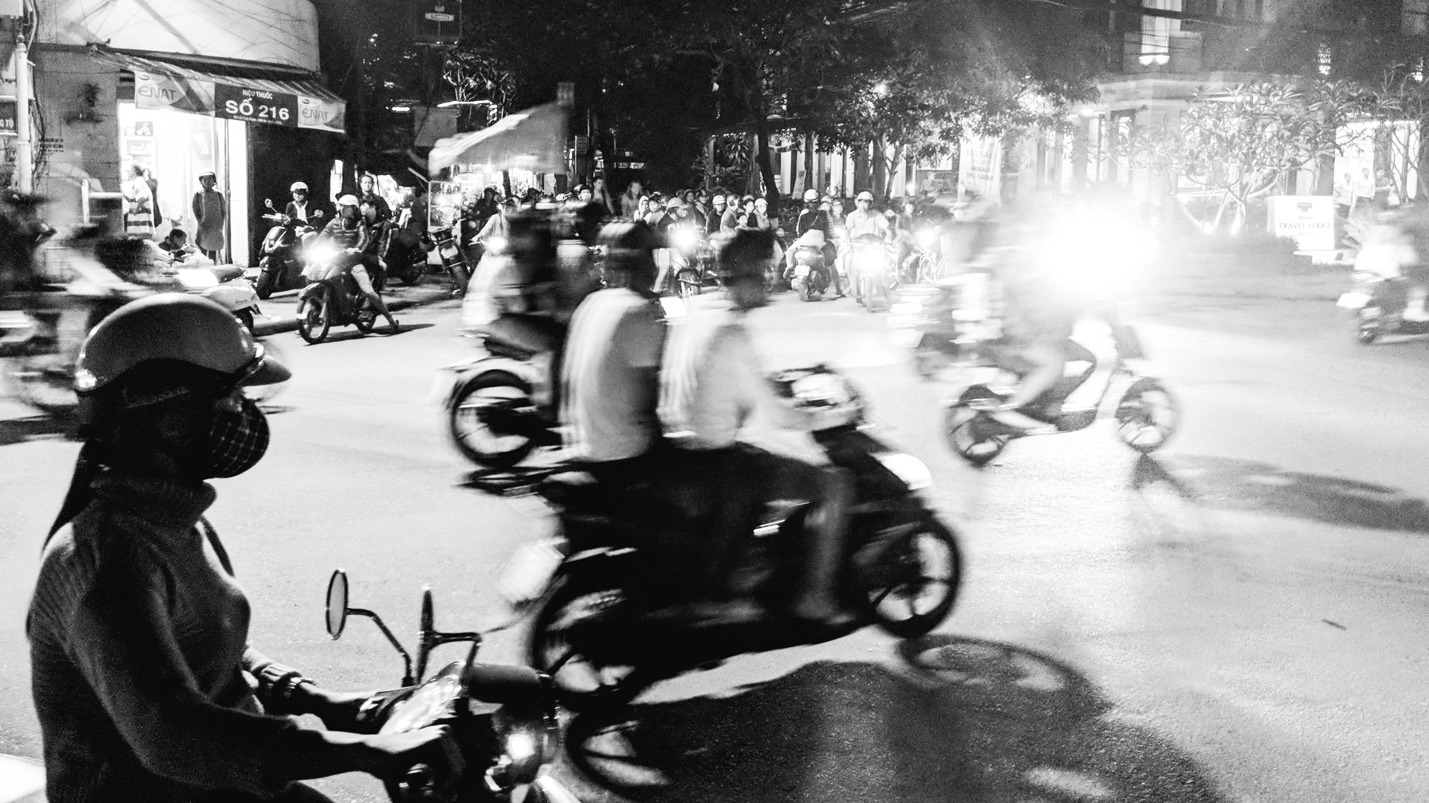 Black and white photo of a busy street at night in Vietnam, with many people on motorbikes.