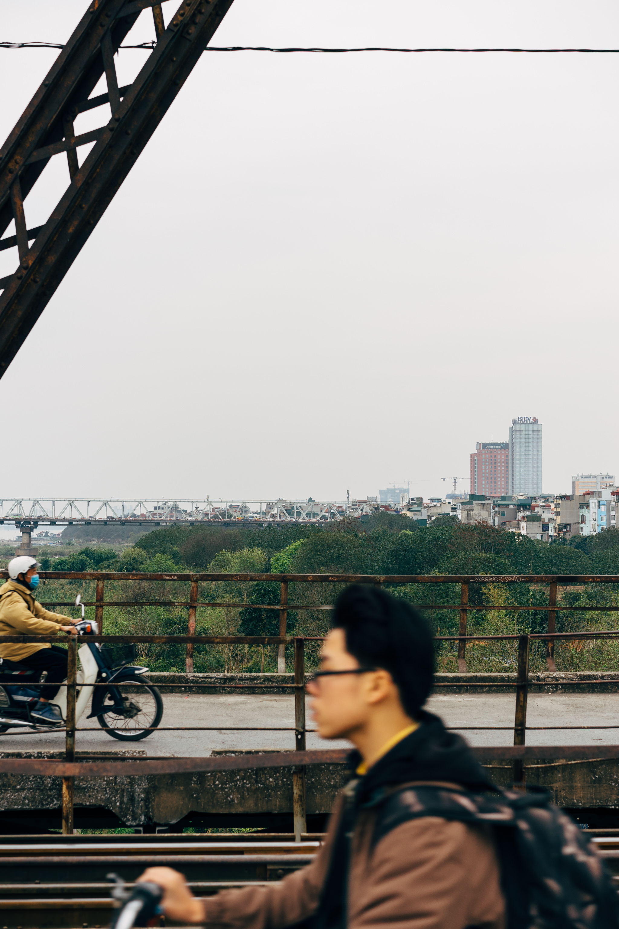 Person on scooter driving on bridge with city skyline in background.