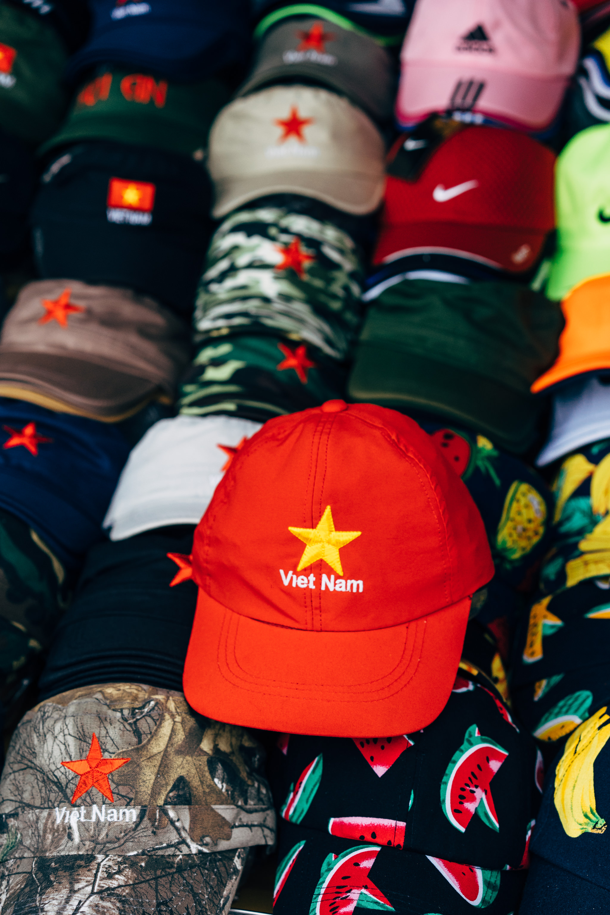 Red baseball cap with yellow star and 'Viet Nam' embroidered on it, among other caps.