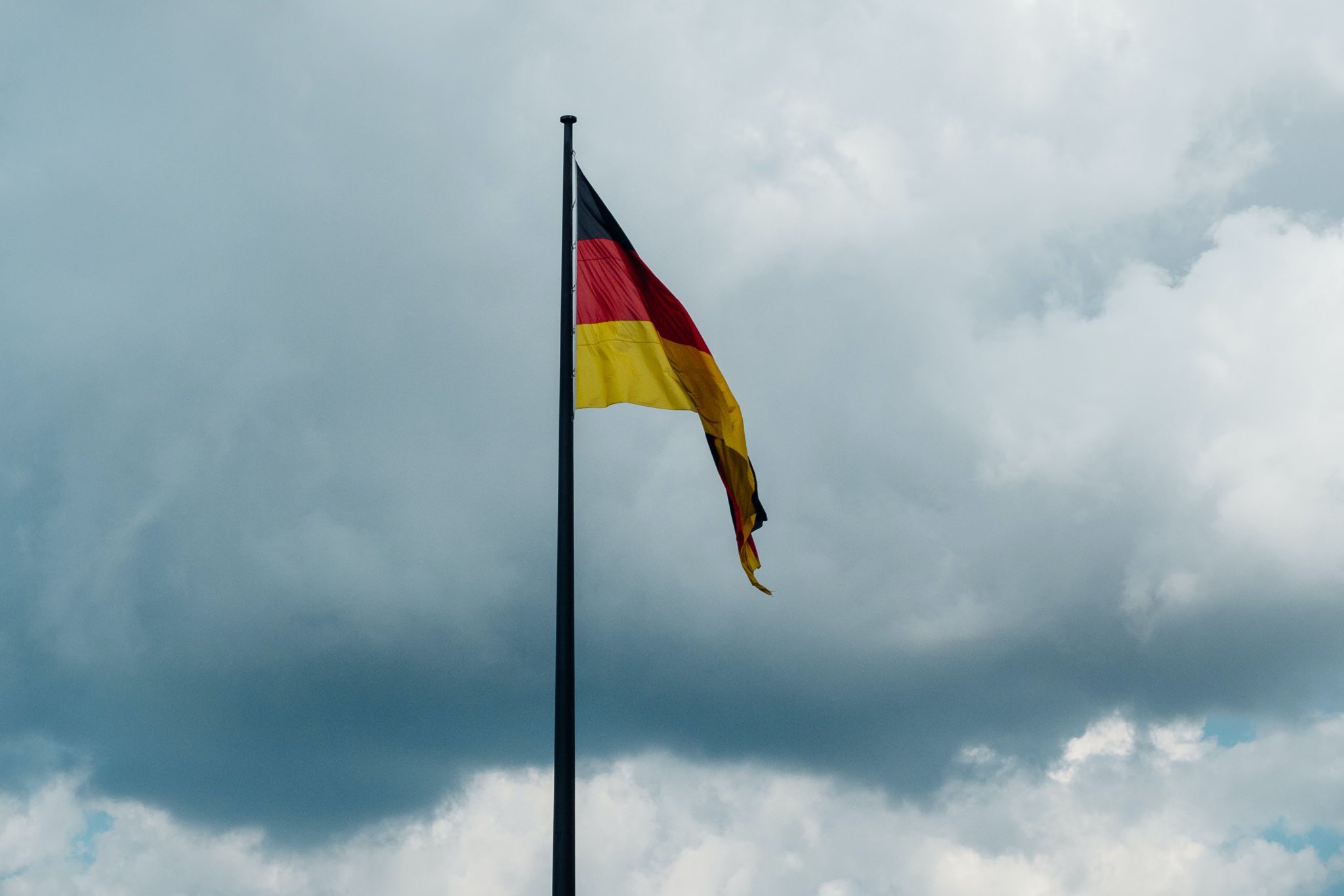 German flag flying from a flagpole against a cloudy sky.