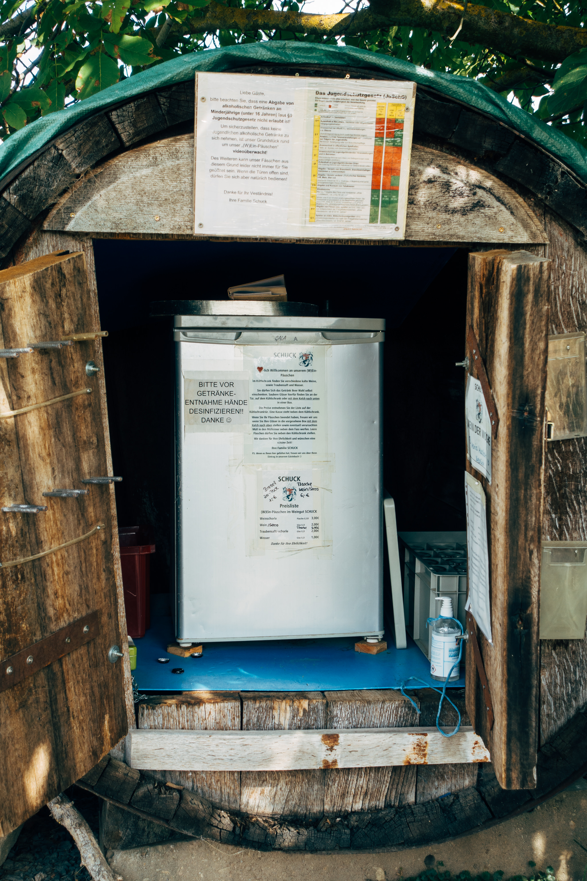 Refrigerator in a wooden barrel-shaped kiosk with signs indicating drink prices and hygiene instructions.