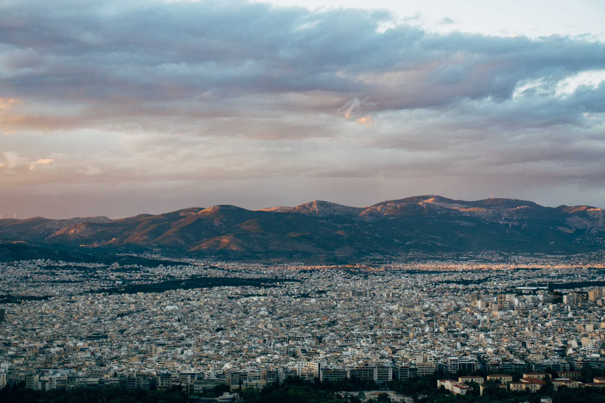 Athens cityscape at sunset with mountains in the background.