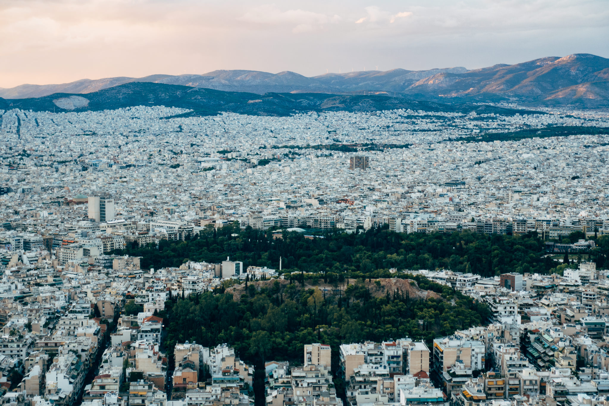 Aerial view of Athens, Greece, showing a large city with a green park and mountains in the background.