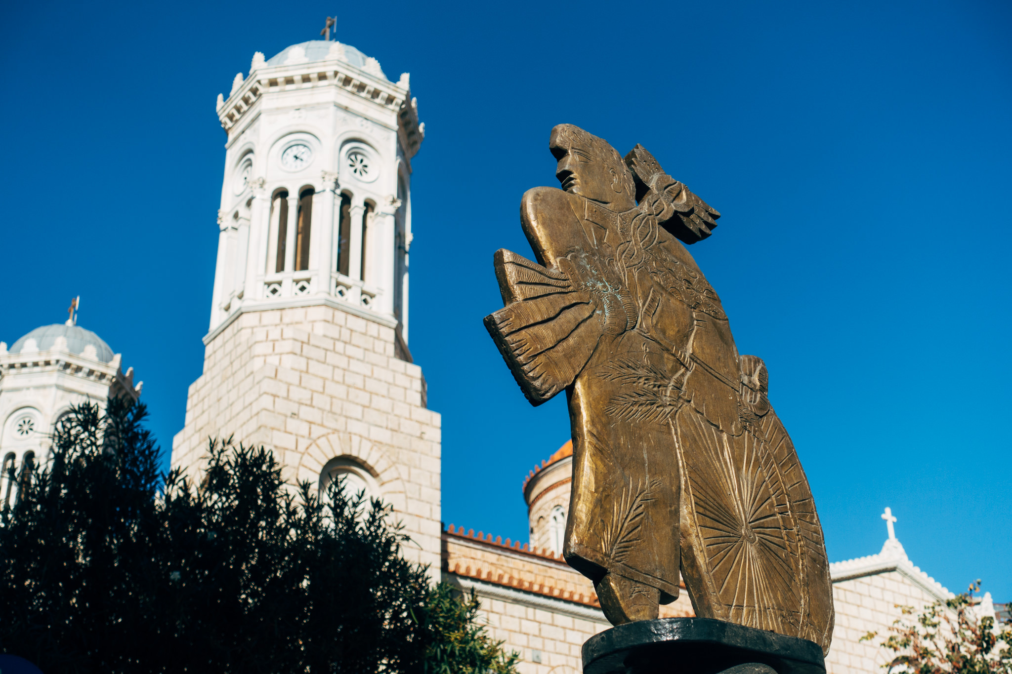 Bronze statue of a winged figure in front of an Orthodox church.