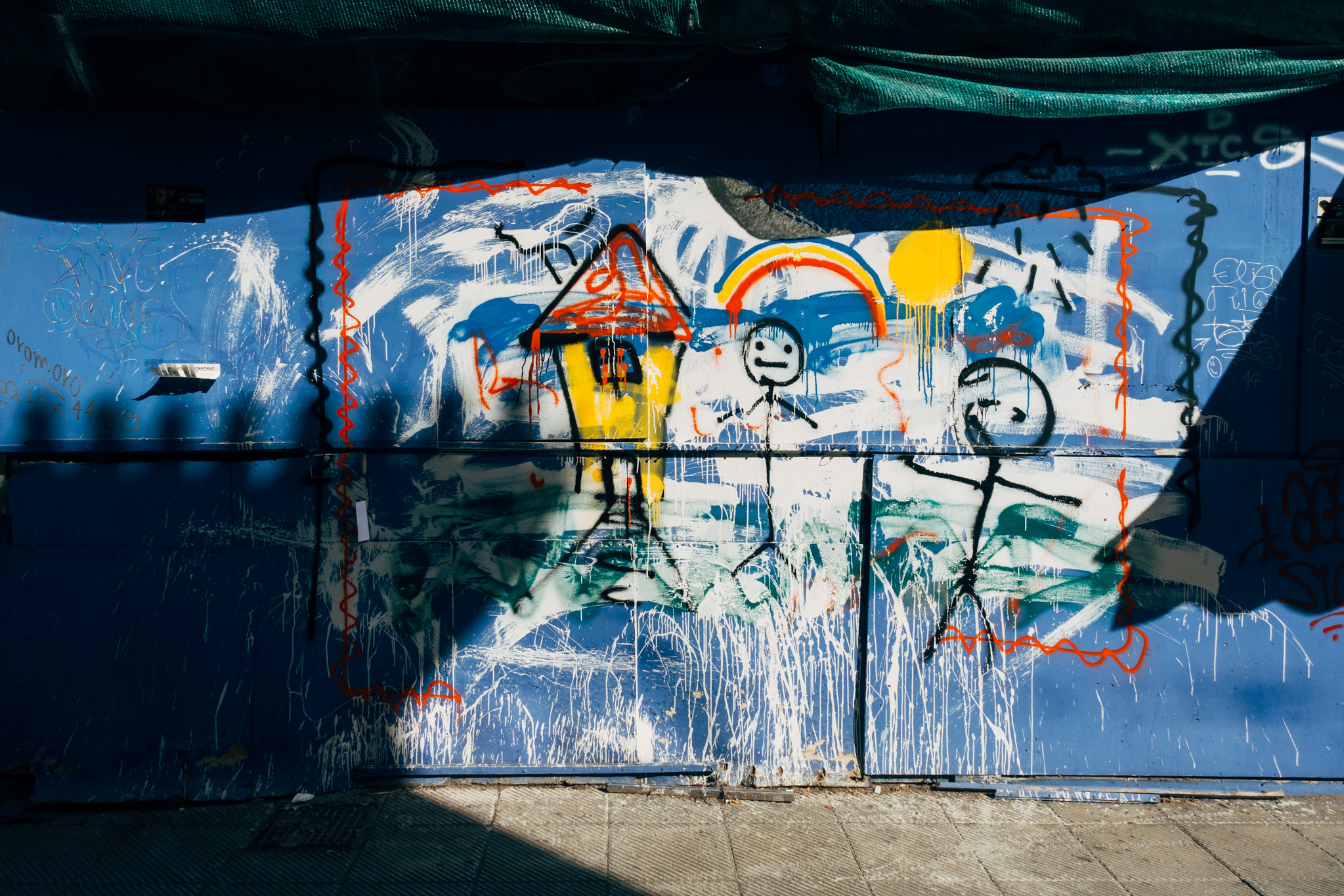 Graffiti-covered blue wall with childlike drawings of a house and figures.