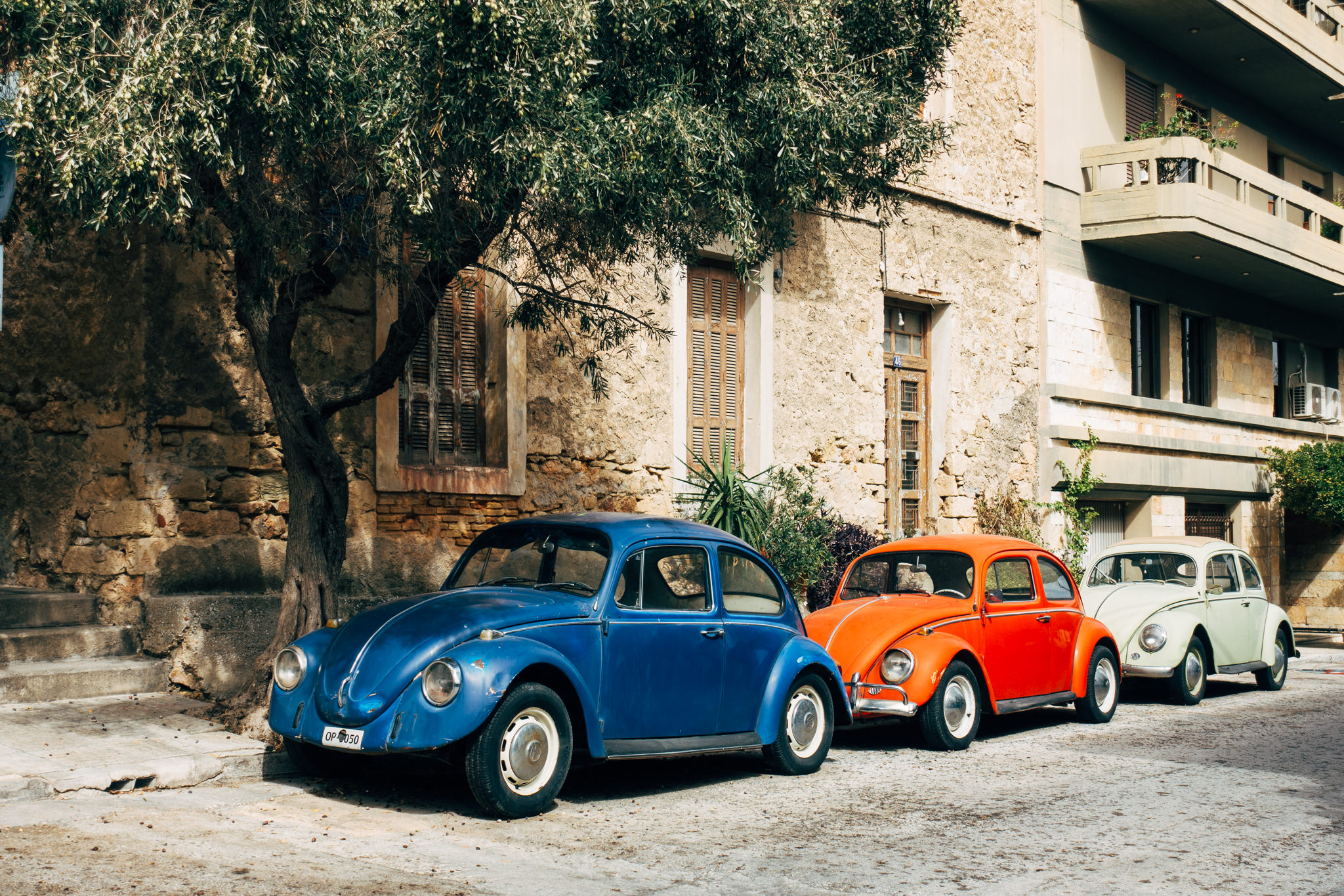 Three vintage Volkswagen Beetles parked in a row, blue, orange, and light green.