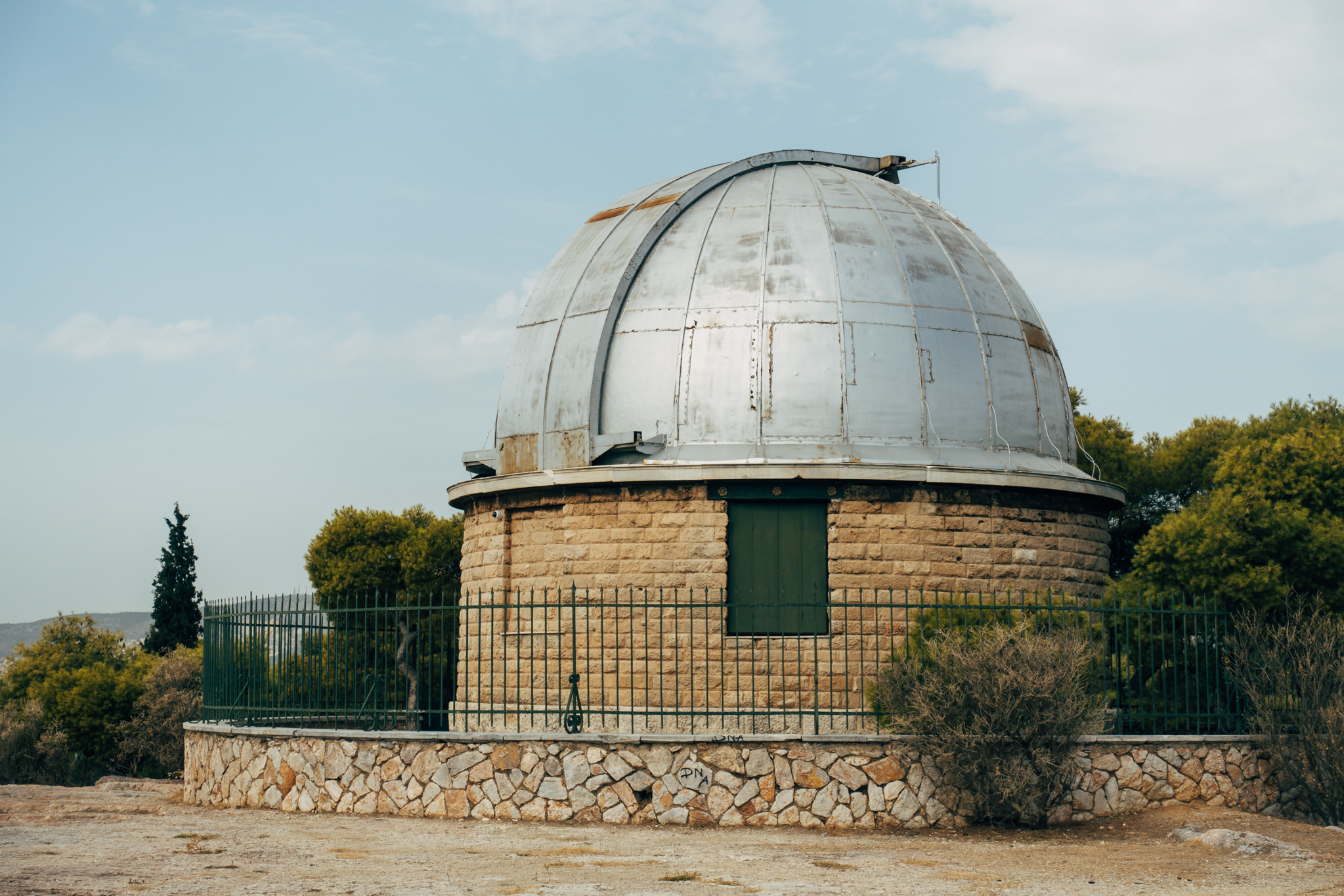 Stone observatory with a metal dome, surrounded by a fence.