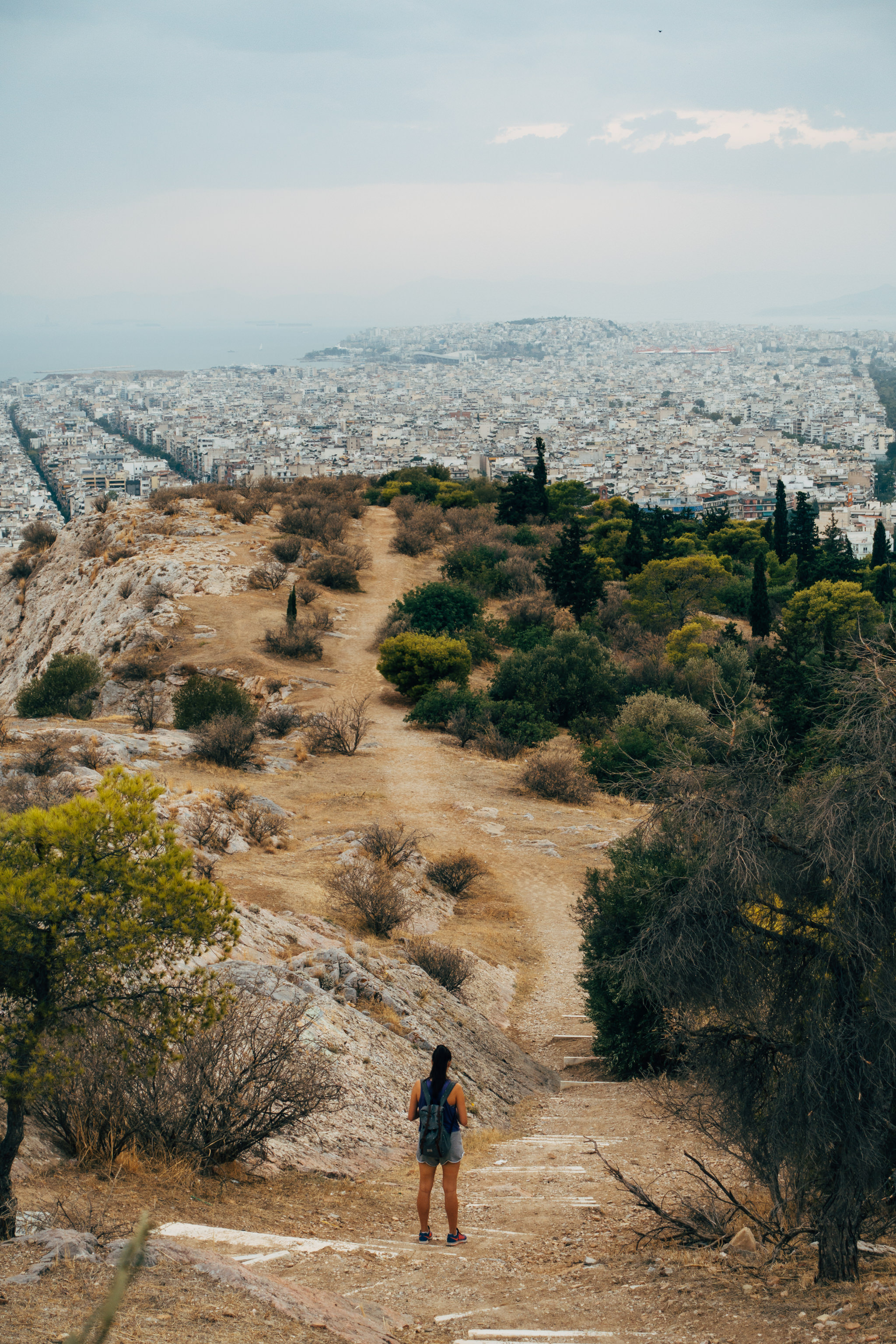 Woman with backpack standing on Filopappou Hill overlooking Athens.