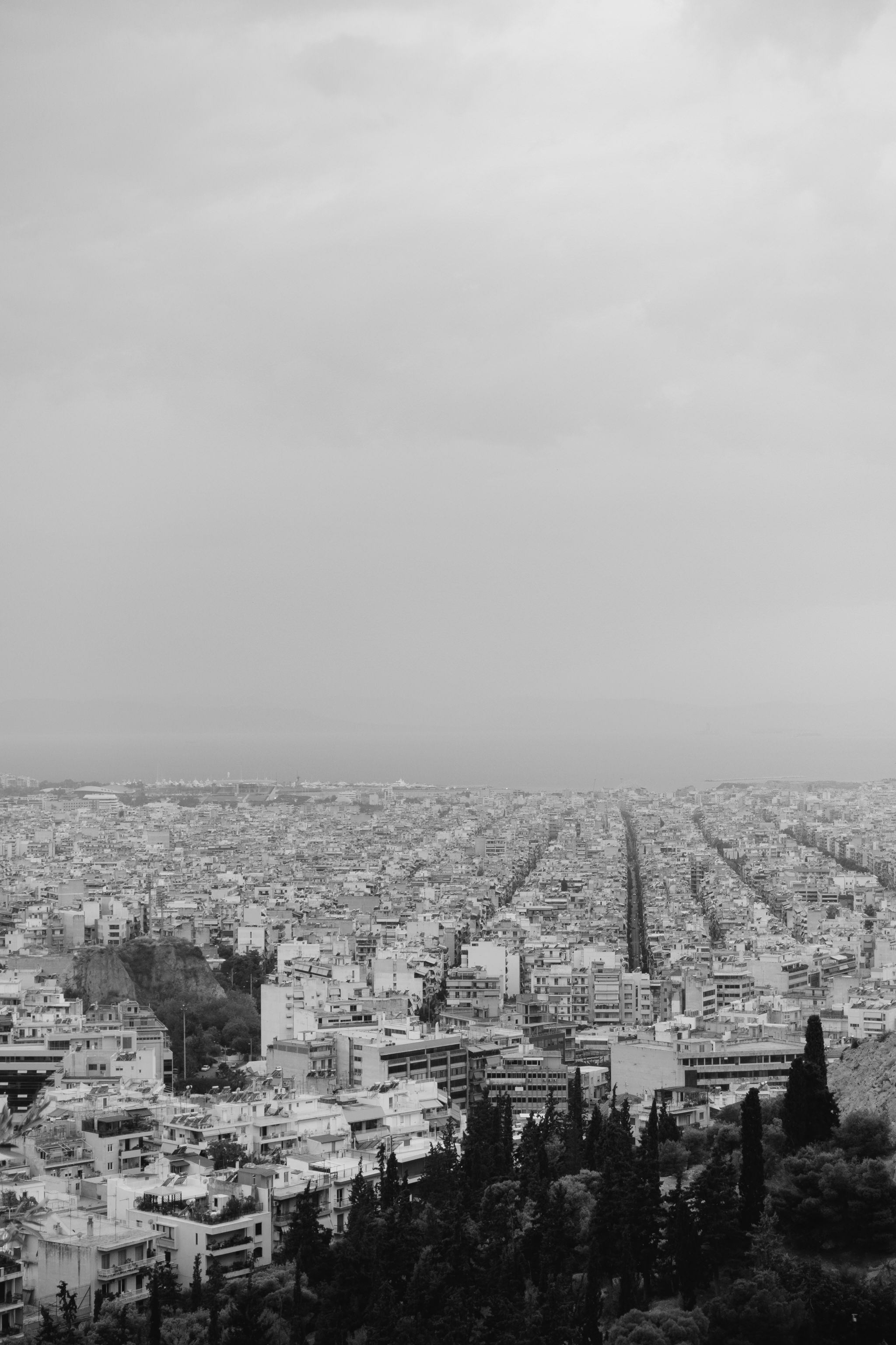 Black and white aerial view of Athens, Greece, showing a dense cityscape extending to the sea.