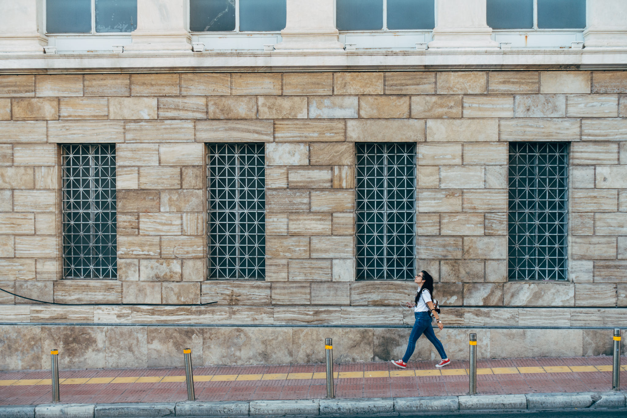 Woman walking past stone building.