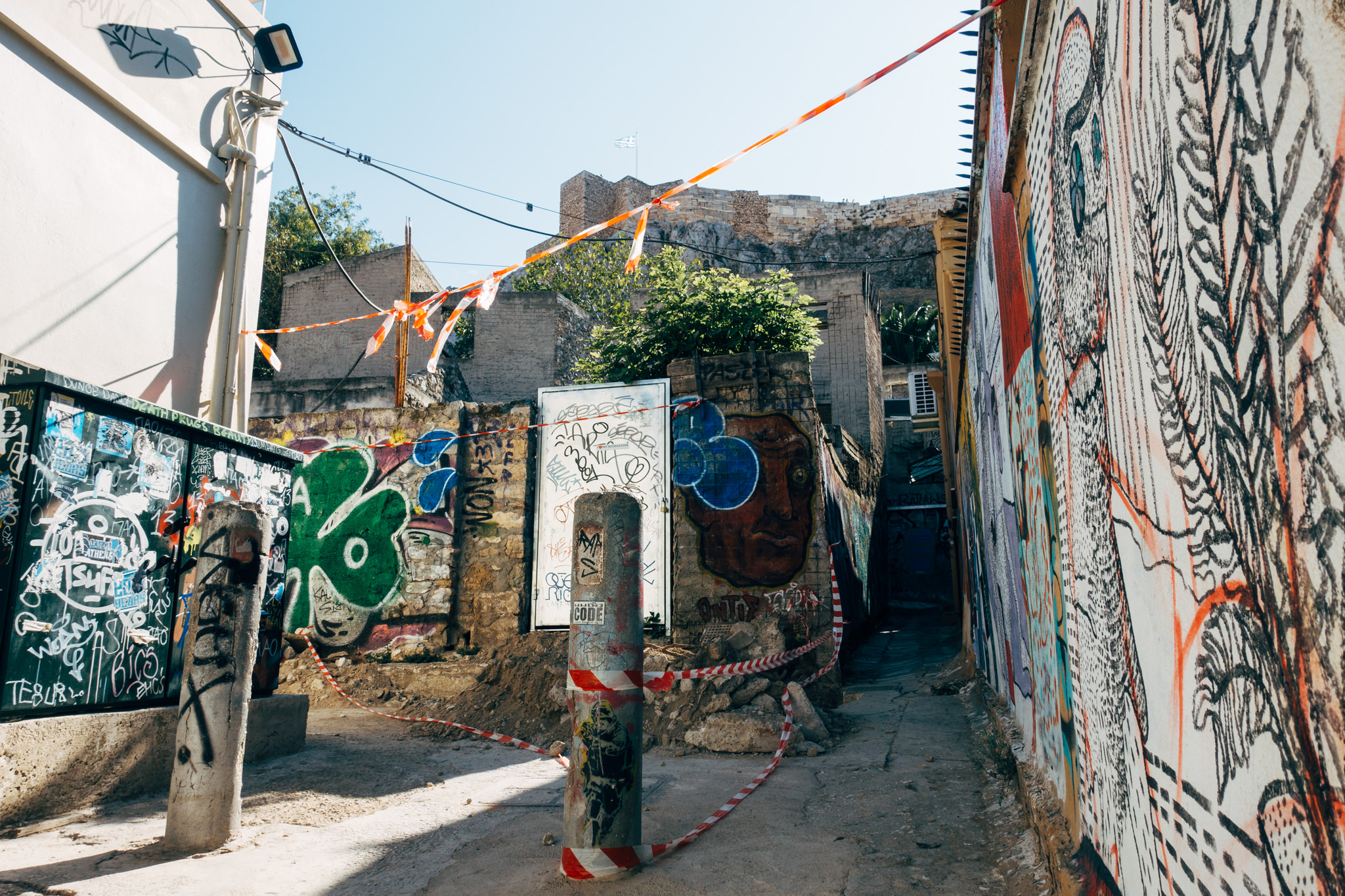 Graffiti-covered alleyway in Athens, Greece, with red and white caution tape.